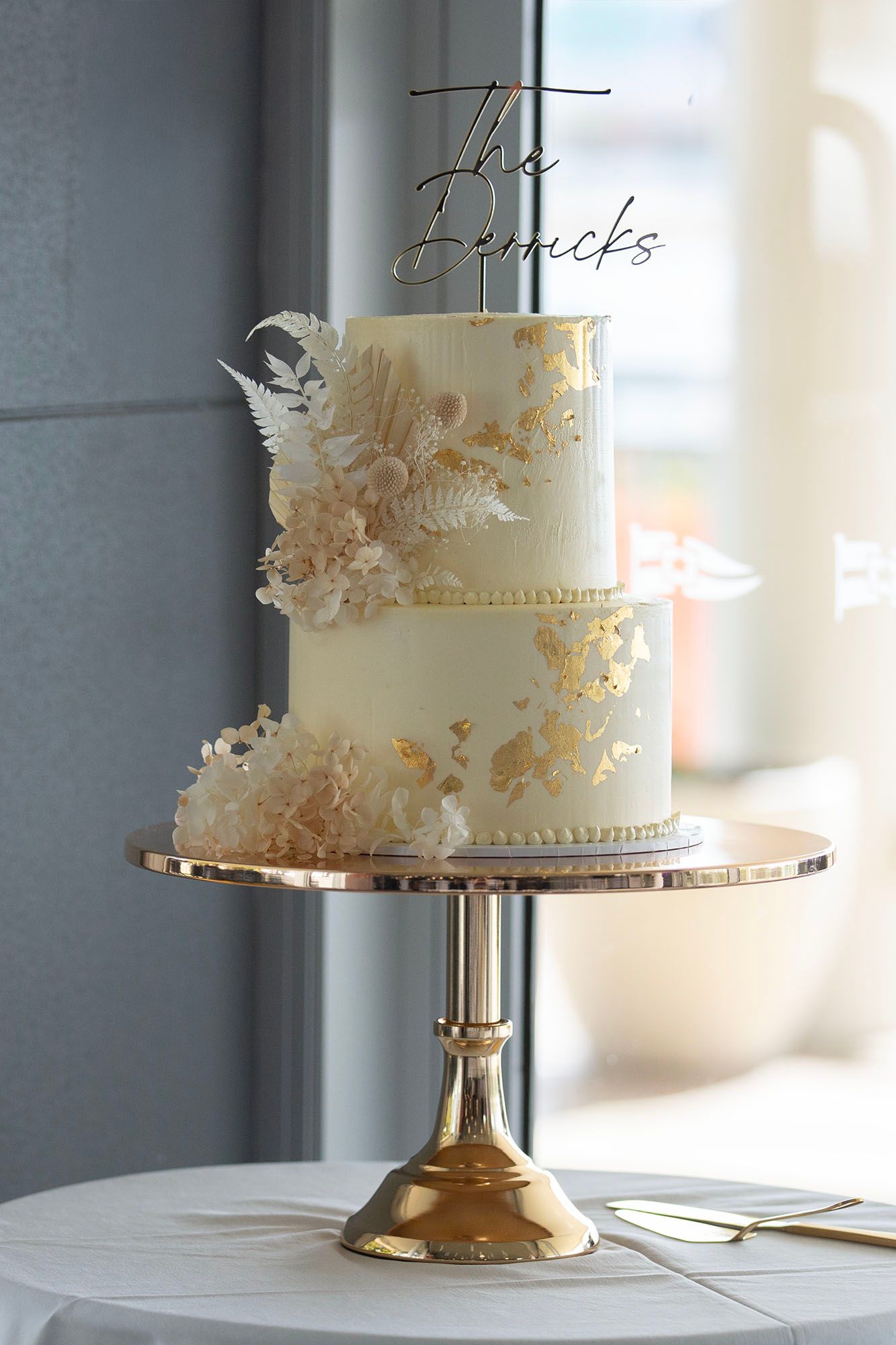 Elegant white wedding cake with delicate floral details on gold metallic cake stand.