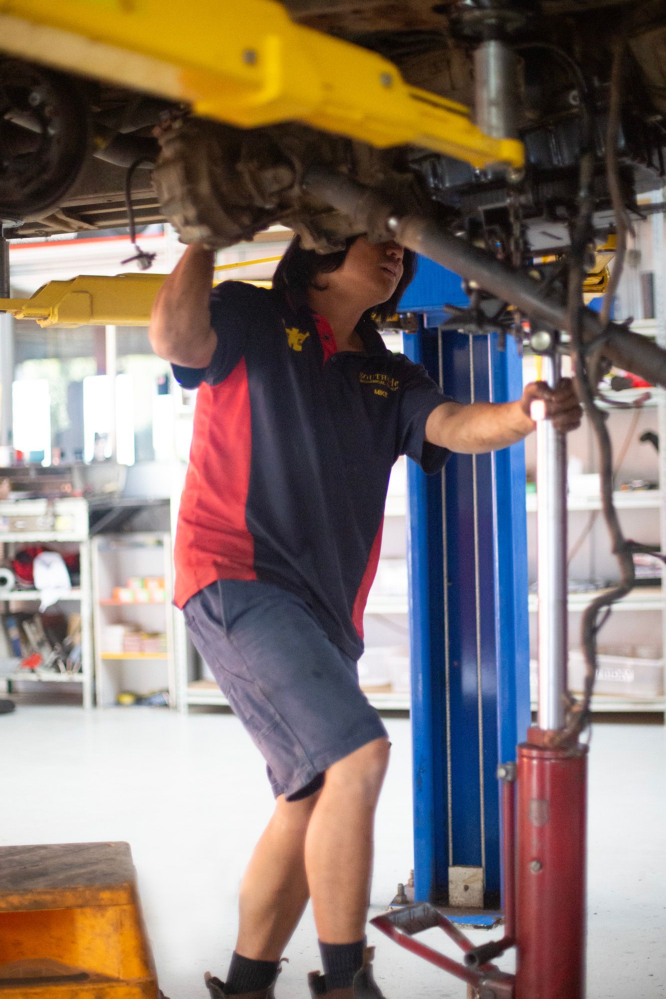 Mechanic working underneath raised vehicle in professional auto service bay.