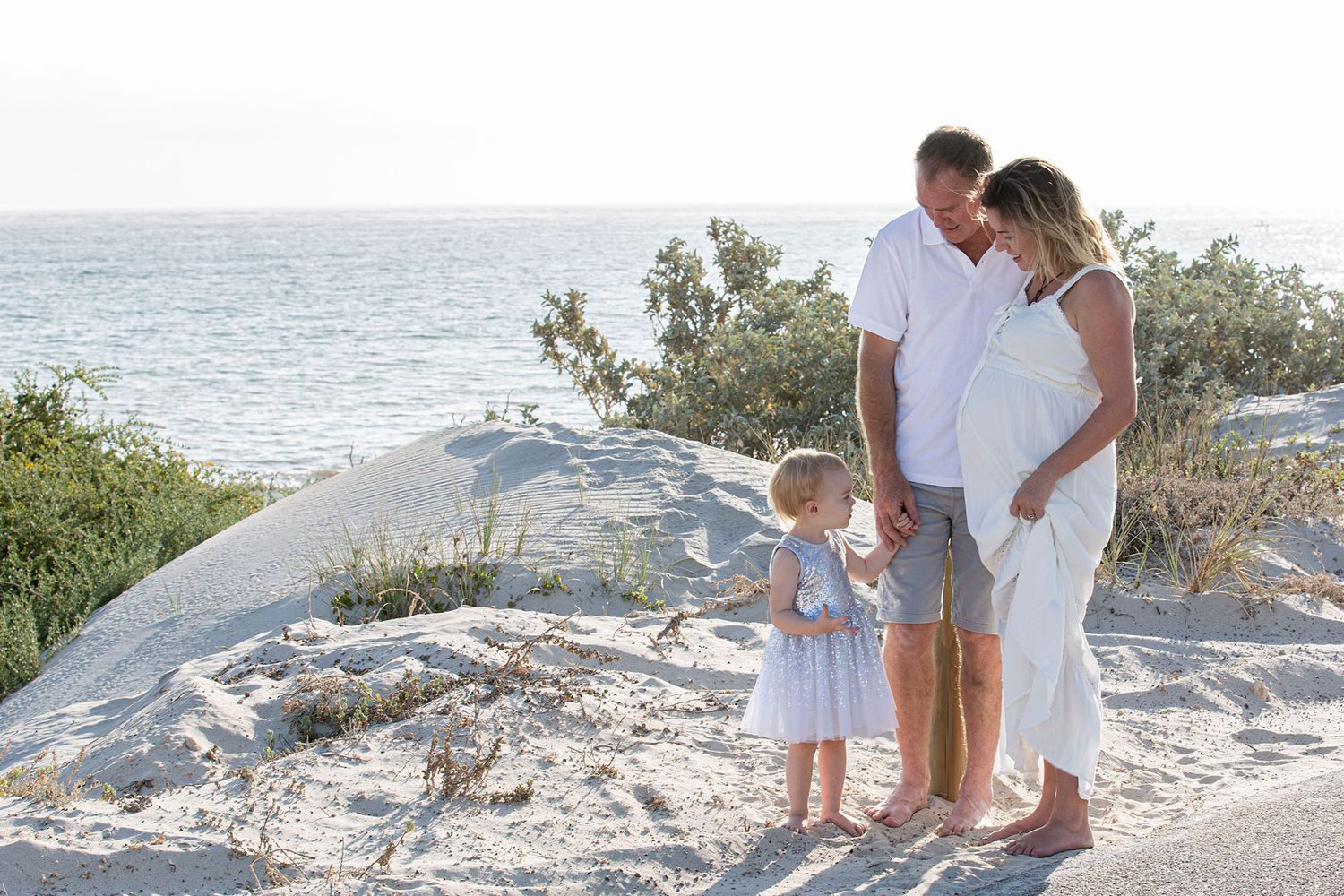 Family shares tender moment on sandy beach overlook with ocean view at sunset.