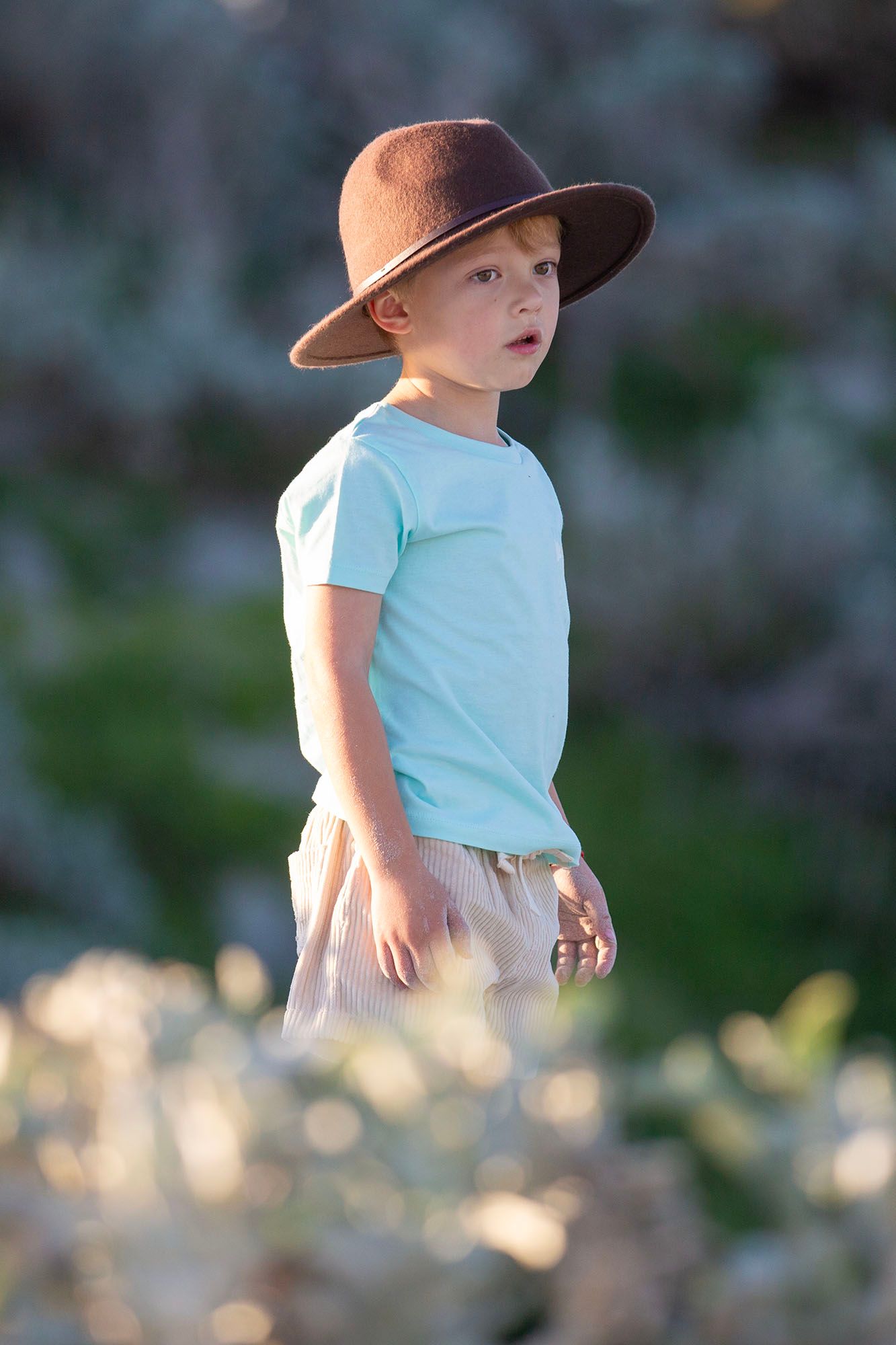 Child wearing sun hat and blue shirt against blurred nature background.