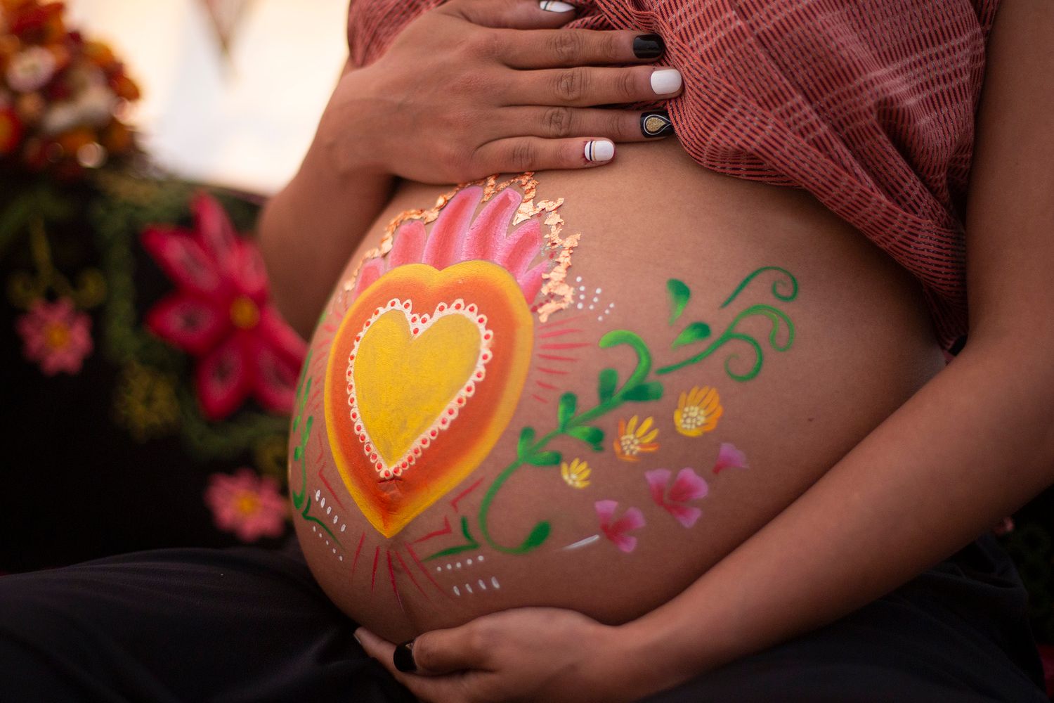 Colorful heart and floral design painted on pregnant belly against dark background.