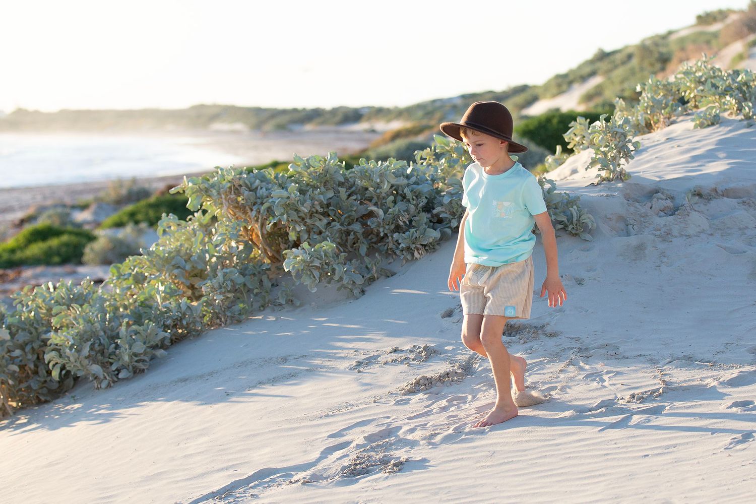 Children playing and running on sandy beach path during golden hour.