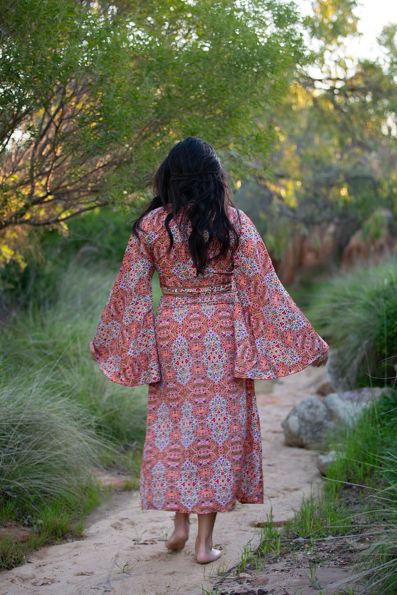 Someone walking through a rustic path wearing a flowing red and white patterned dress.