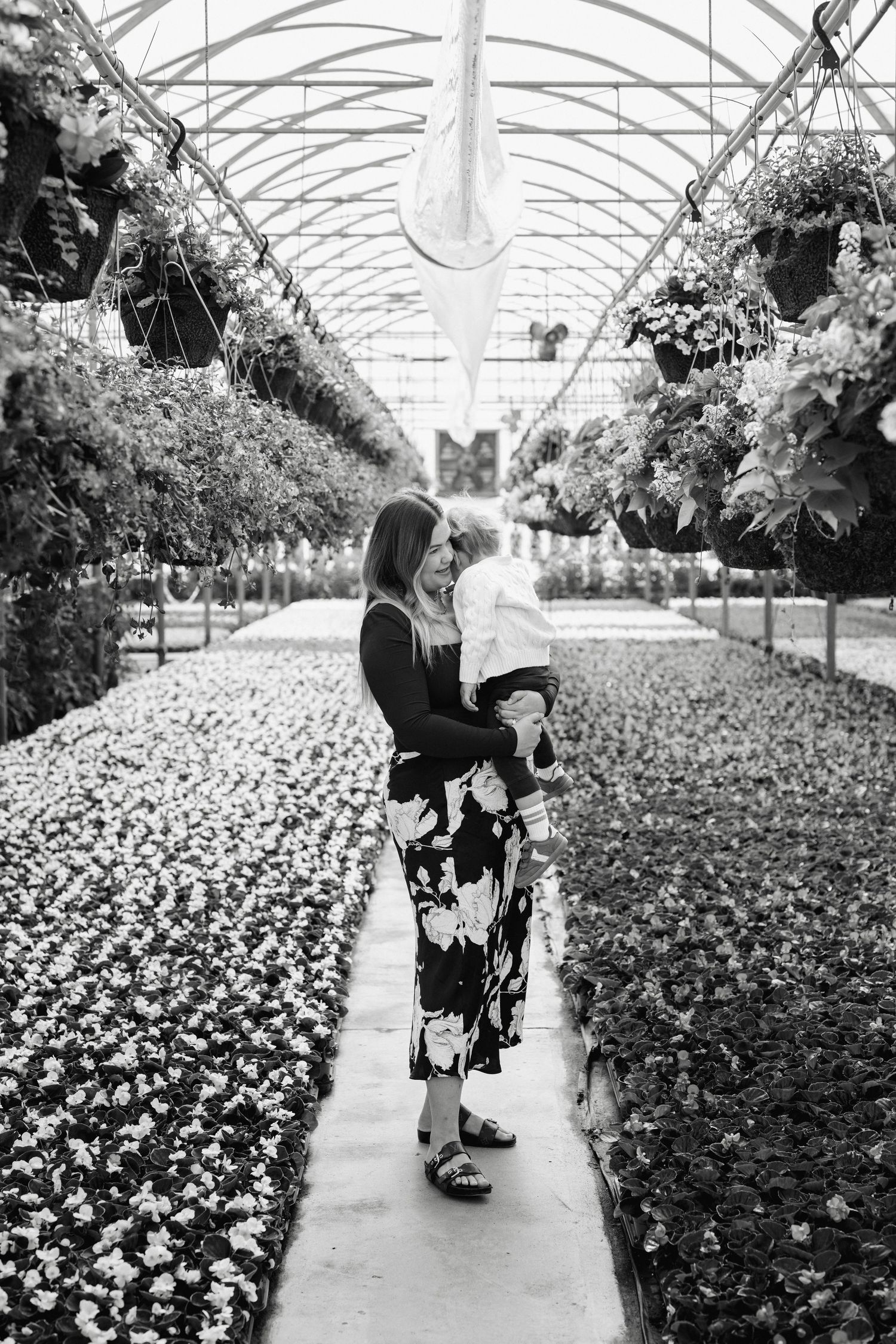Black and white sequence showing people walking through a greenhouse filled with flowers.