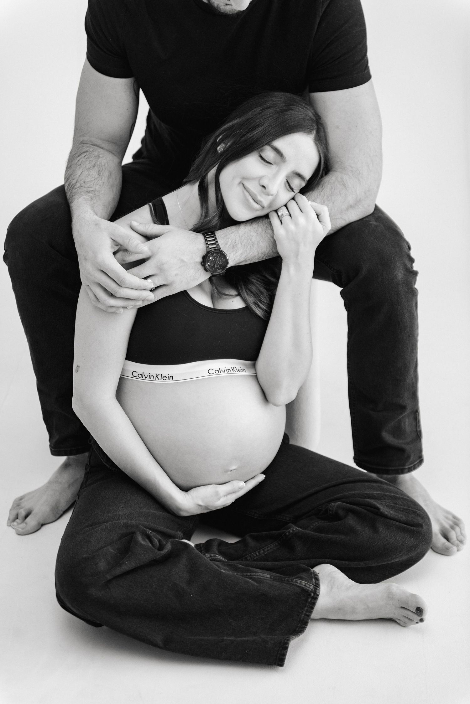 Intimate maternity photography captures couple's connection on white background.