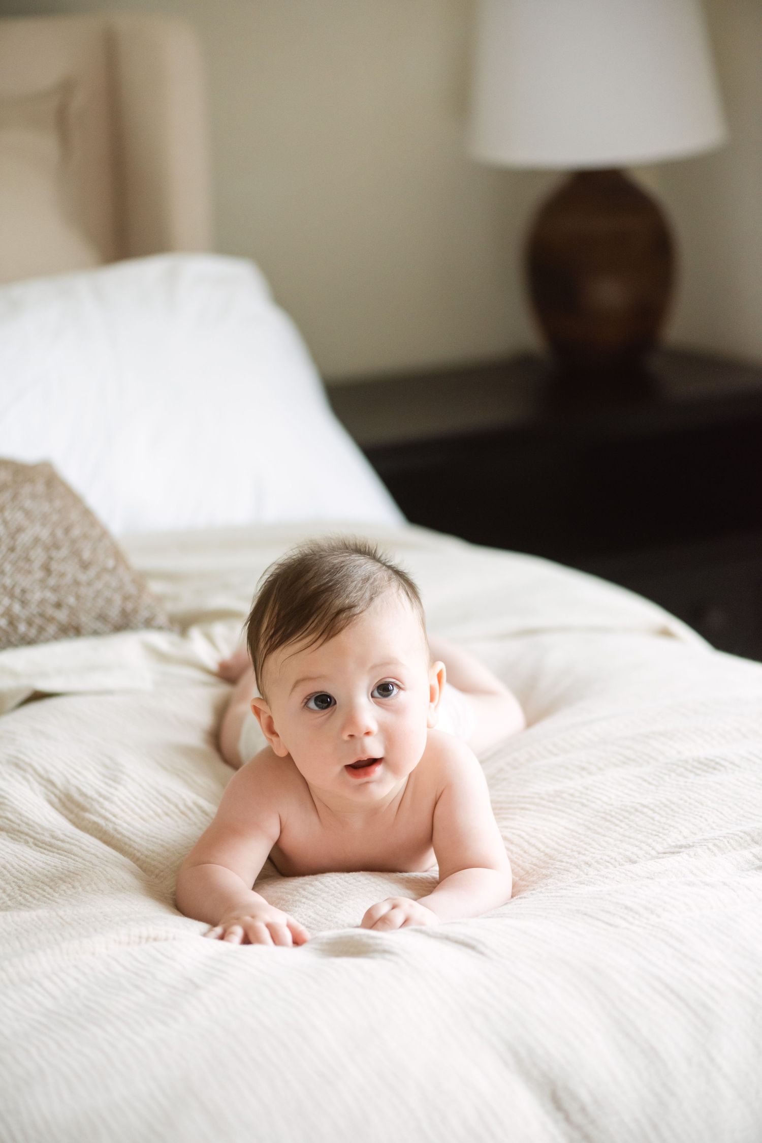 Sweet baby lying on white bedding in natural light during lifestyle newborn photography session.