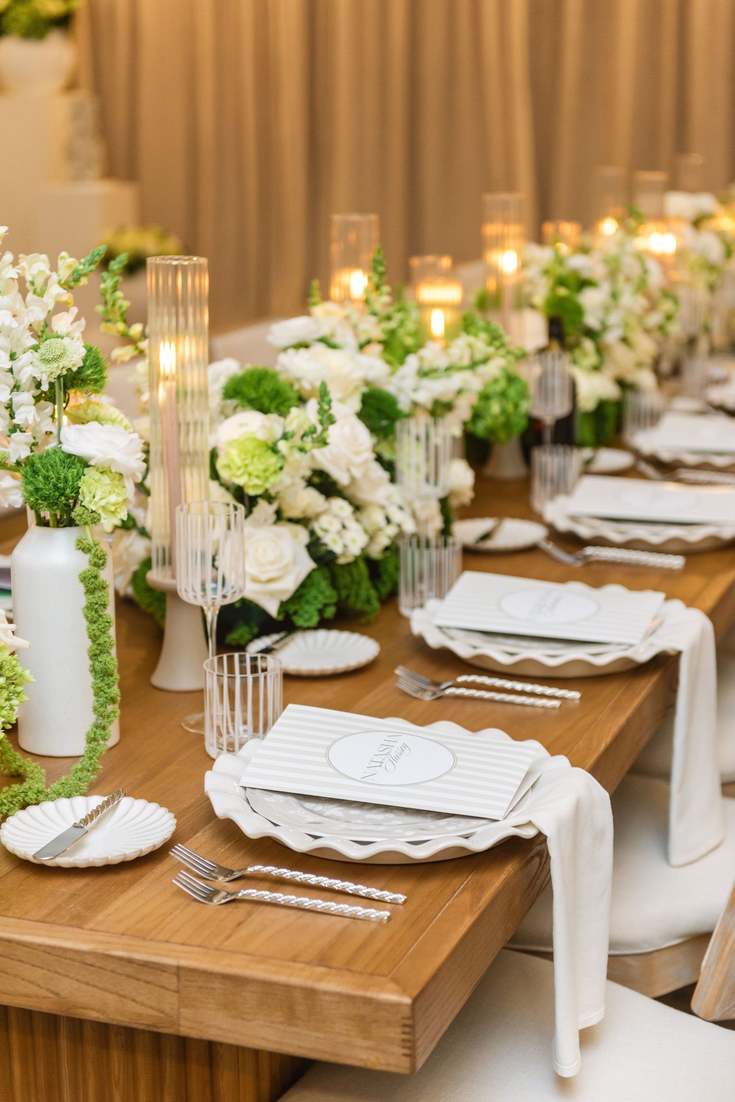 Wedding table decor featuring white flowers, glass candleholders, and elegant place settings.