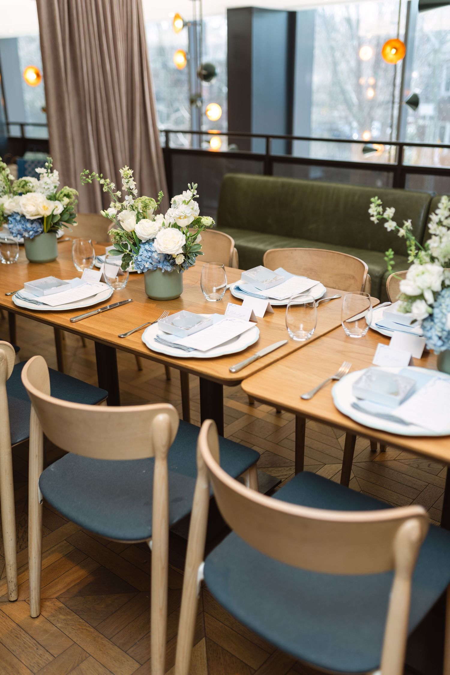 Elegant table settings with white plates and blue chairs in a modern restaurant dining room with floral centerpieces.