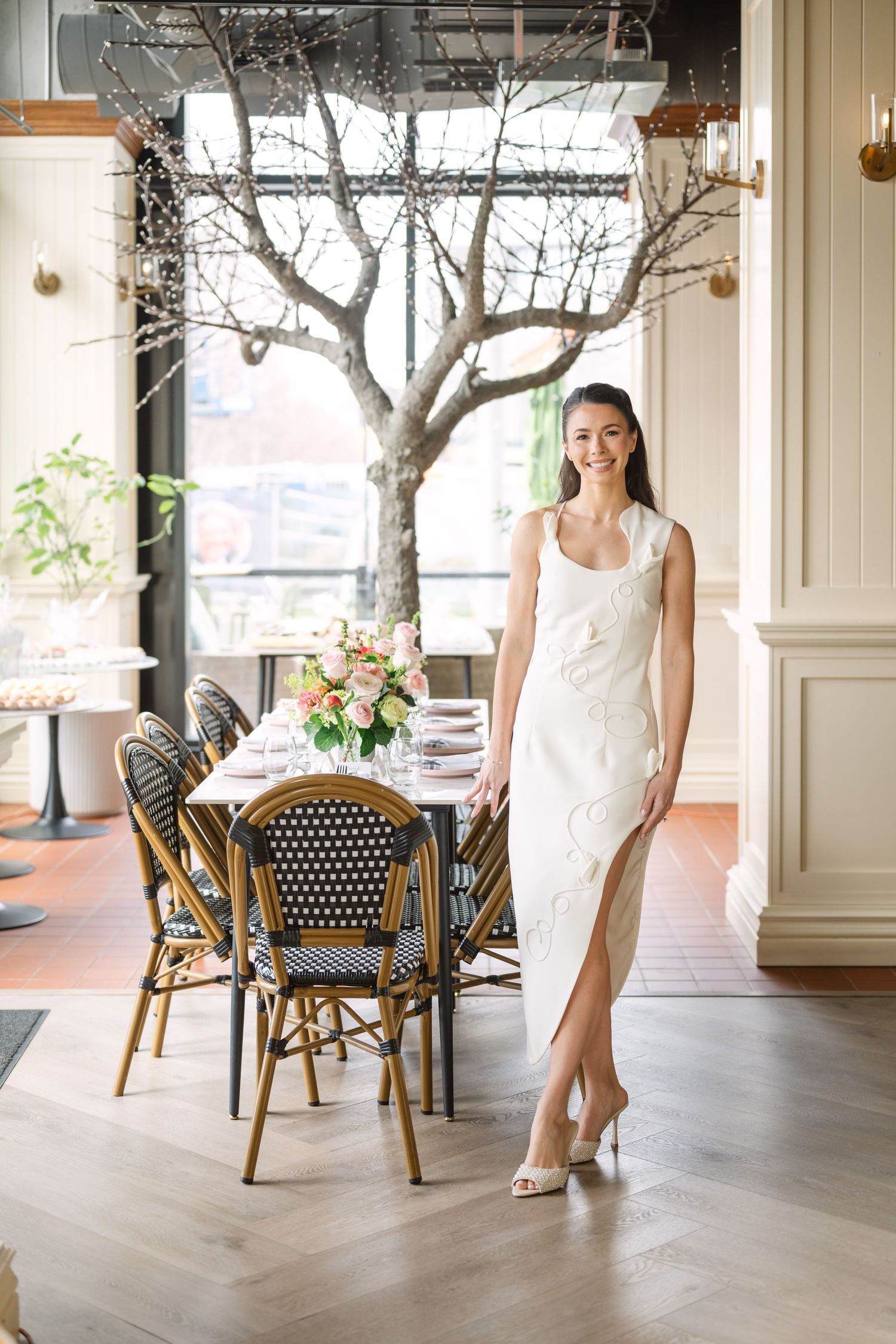 Elegant bride in white dress standing beside a beautifully set dining table with floral centerpiece in a chic venue.