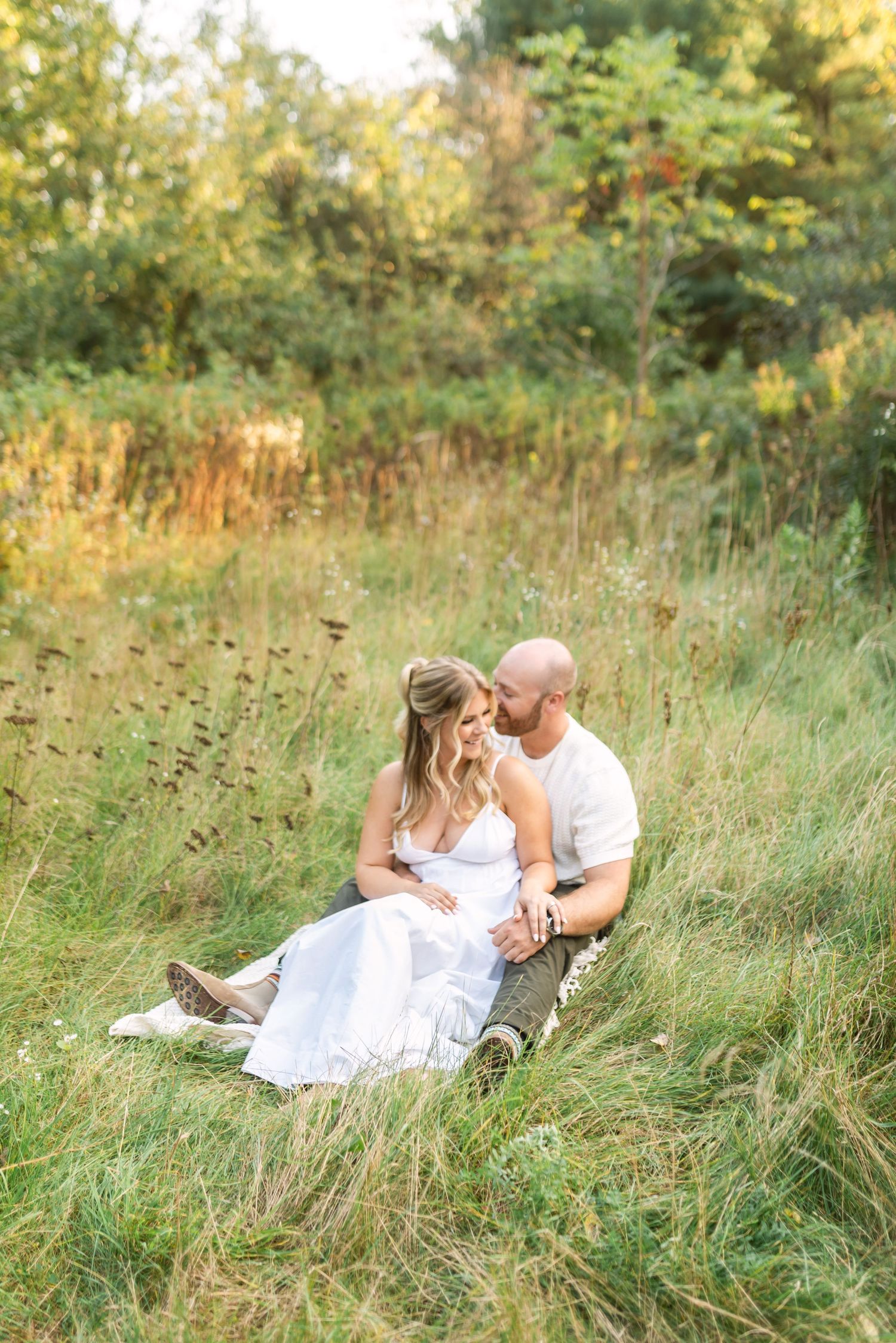 Romantic couple embraces while lying in tall grass during golden hour sunset.