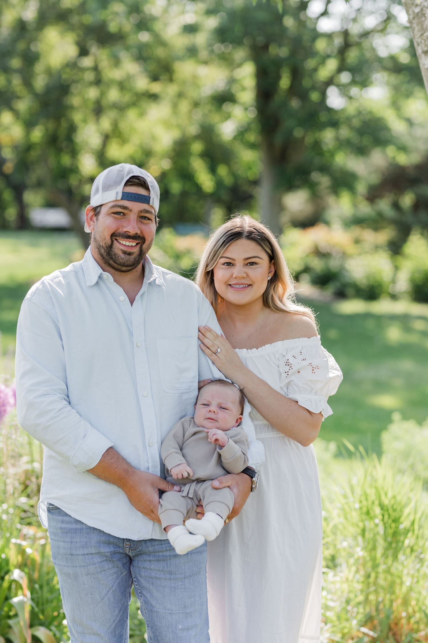 A sunny outdoor family portrait in a lush green garden setting.