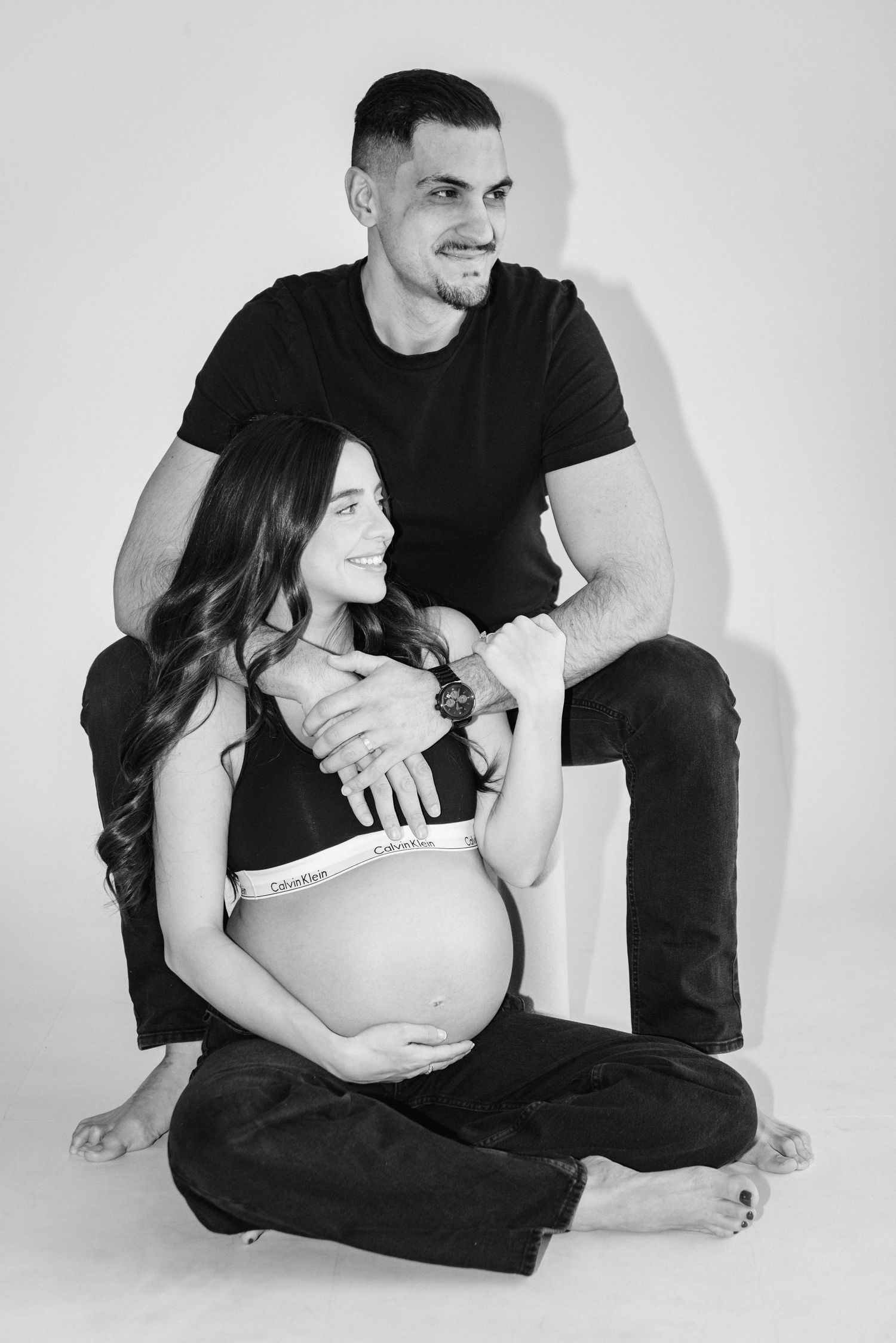 Candid maternity photos show couple's connection in minimalist studio setting.
