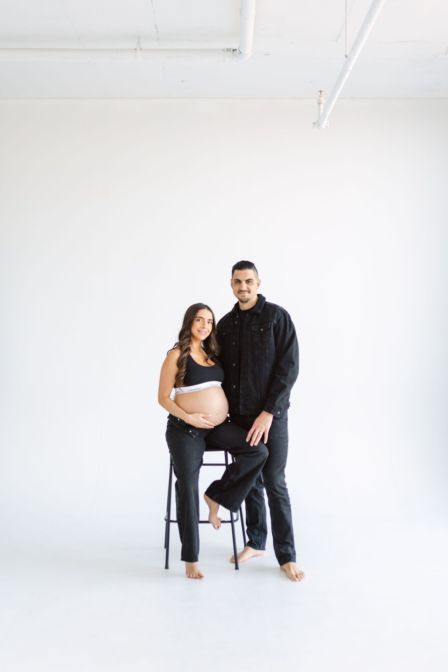Professional studio maternity session with couple posing by chair.