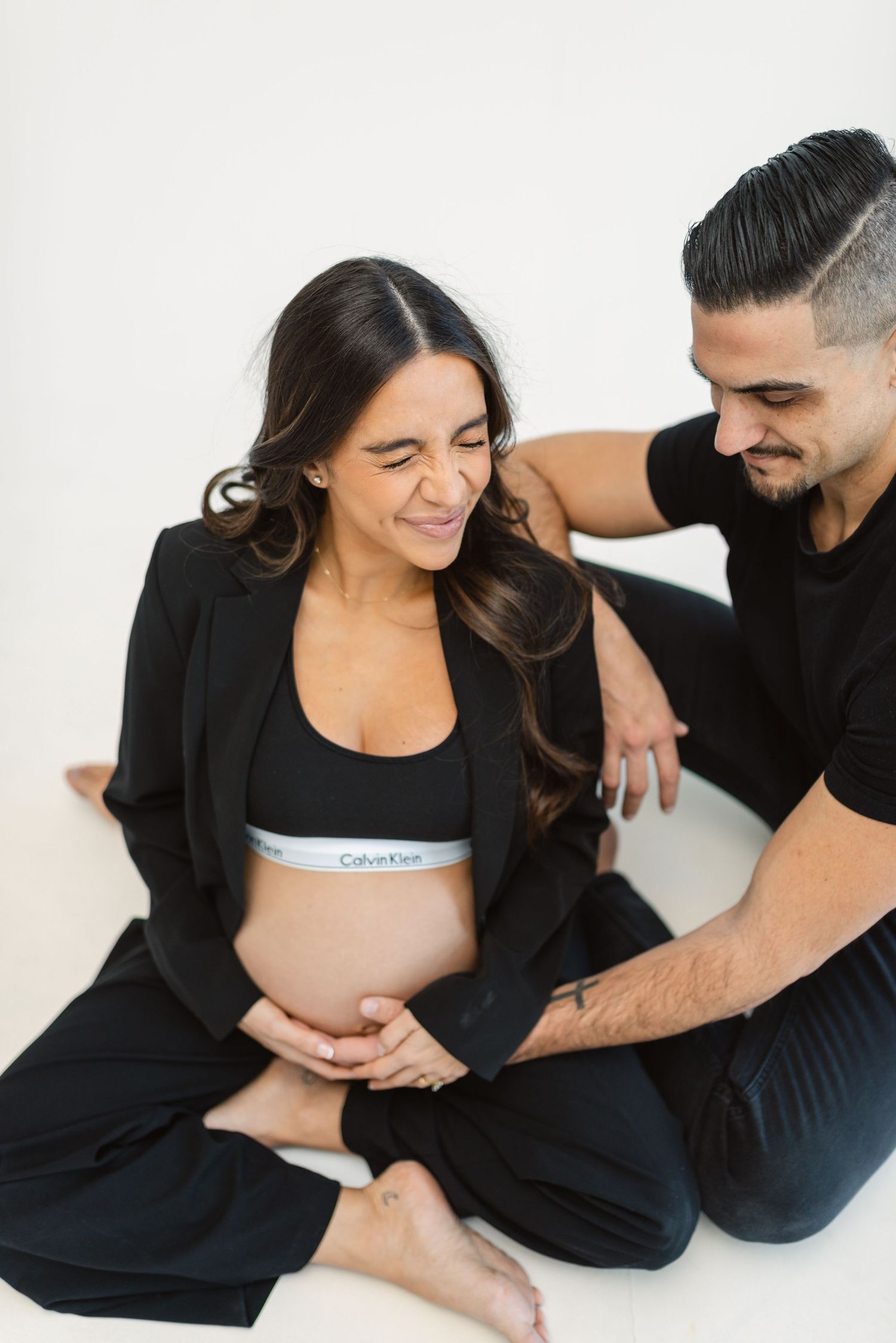 Couple in black clothing poses together on floor during maternity session.