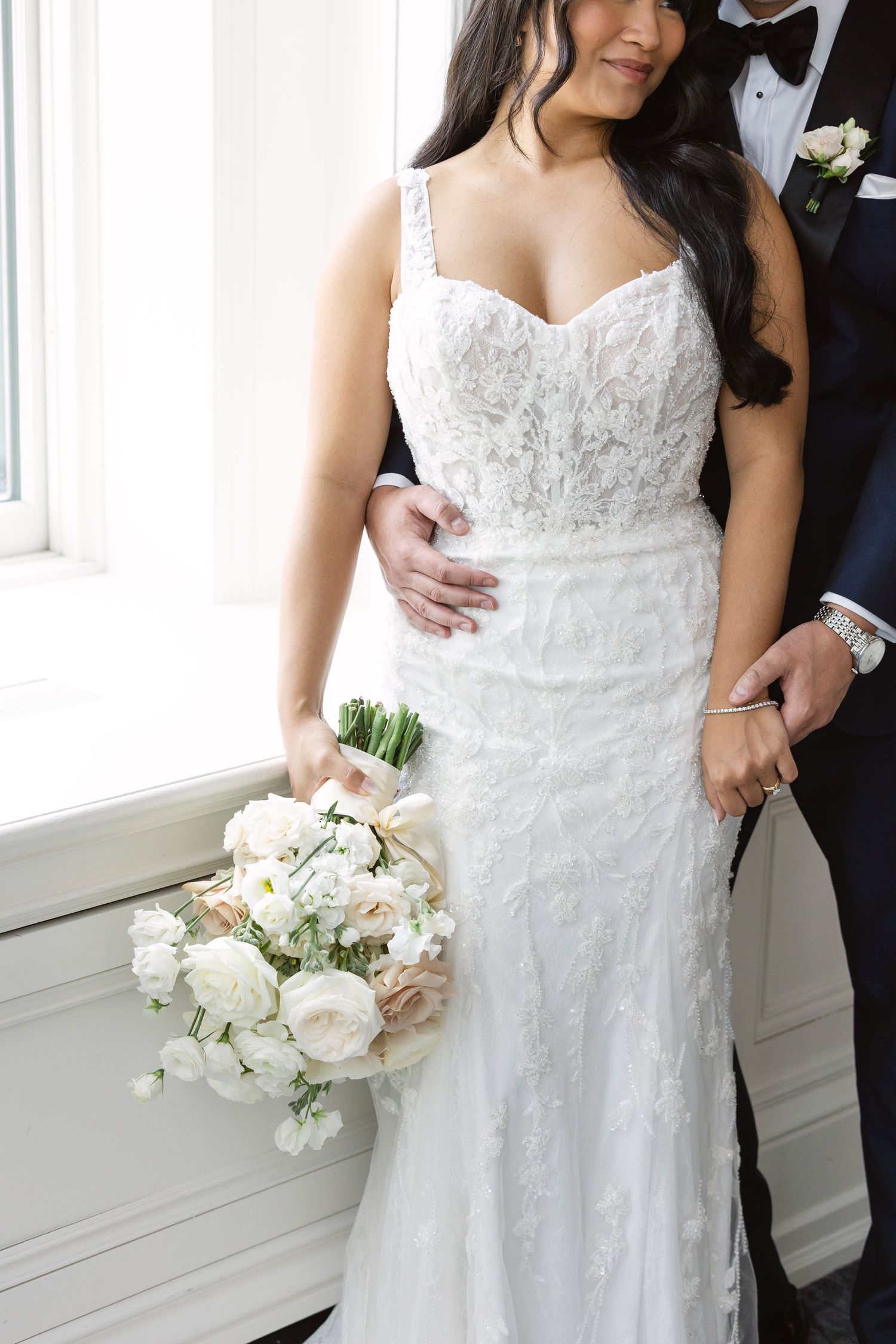 Details of a beautiful lace wedding dress with delicate floral bouquet in an elegant setting.