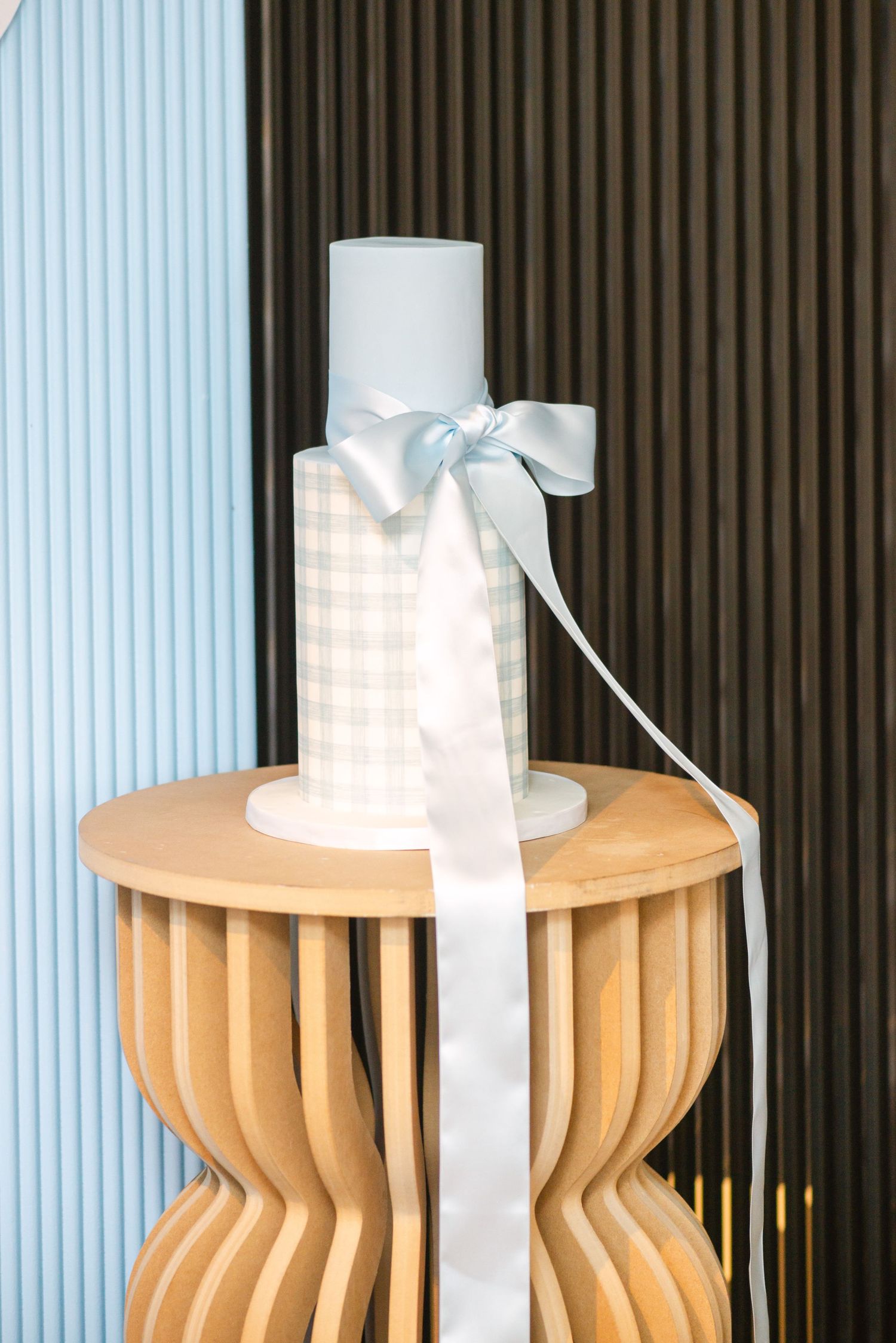 Three decorative wooden stools or side tables with curved ribbed designs sit against a blue striped wall.