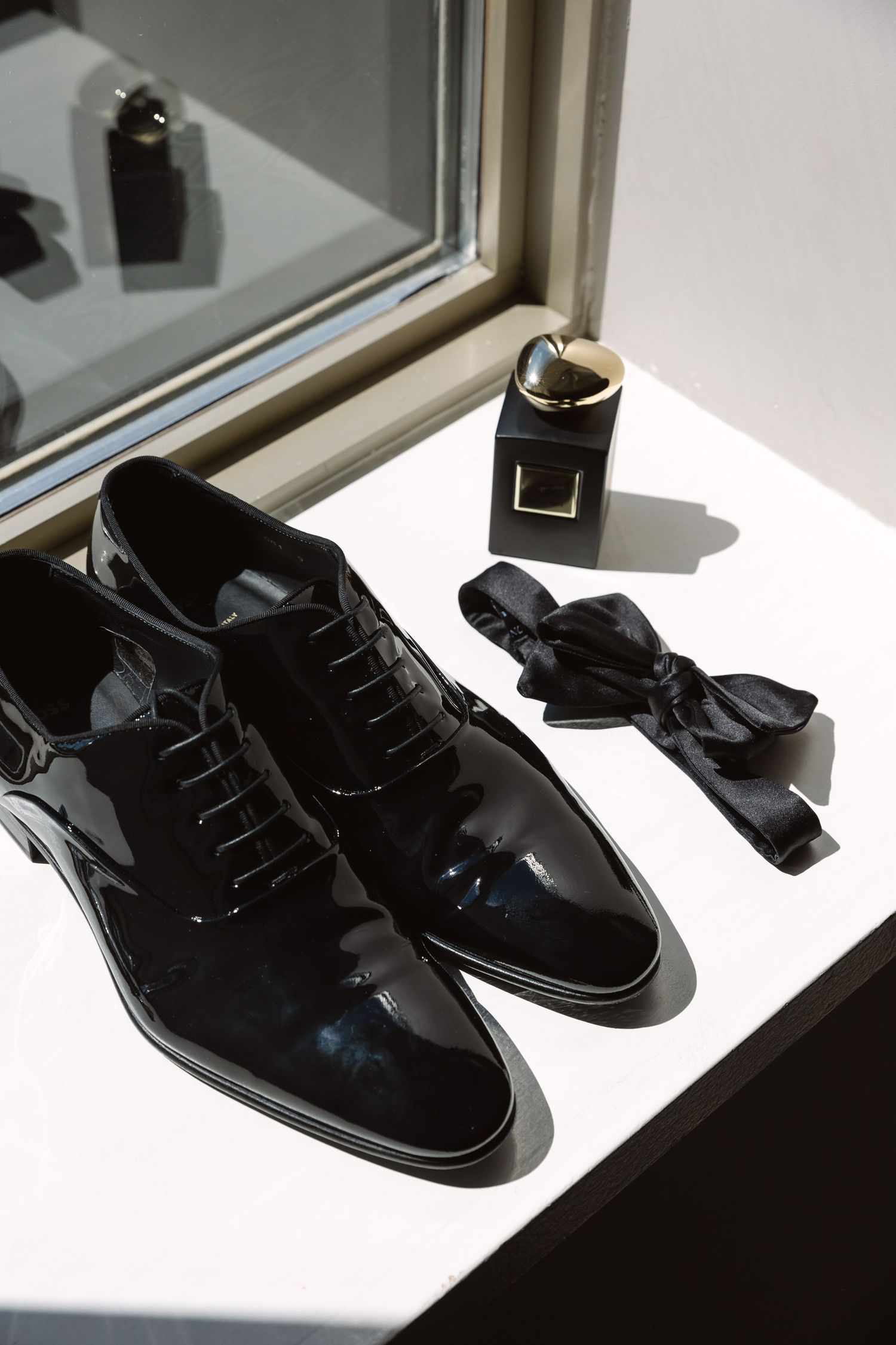 Shiny black dress shoes displayed in a row on a white surface with dramatic lighting and shadows.