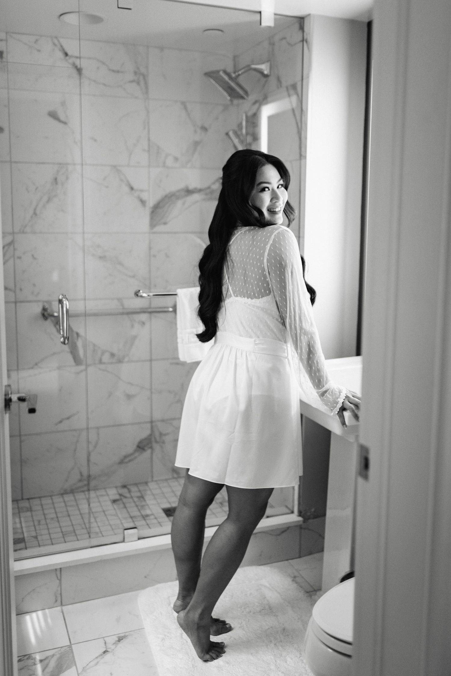 Black and white photo of bridal preparations in a marble bathroom setting.