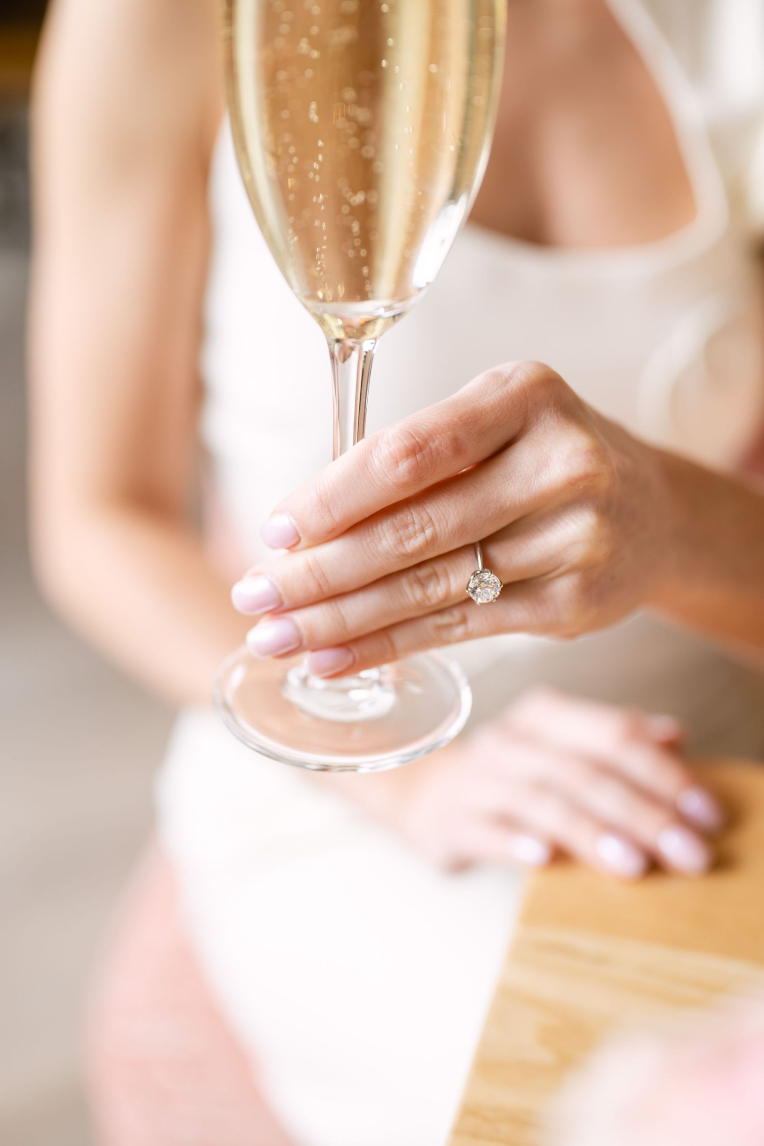 Close-up of a bride's hand wearing a diamond engagement ring while holding a champagne flute.