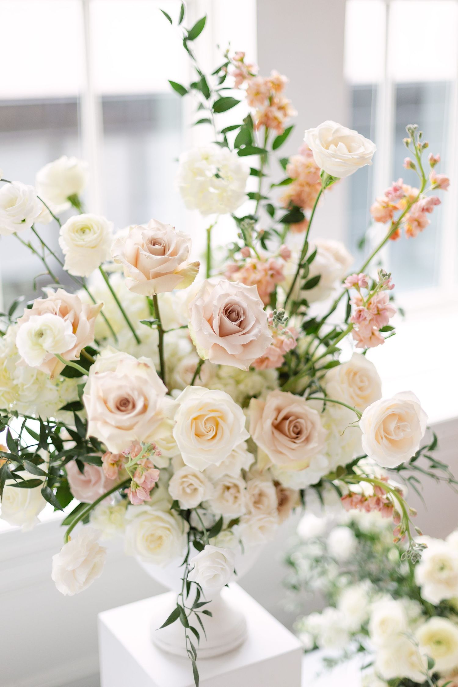 Delicate arrangement of blush roses and white flowers with greenery in classic vases.