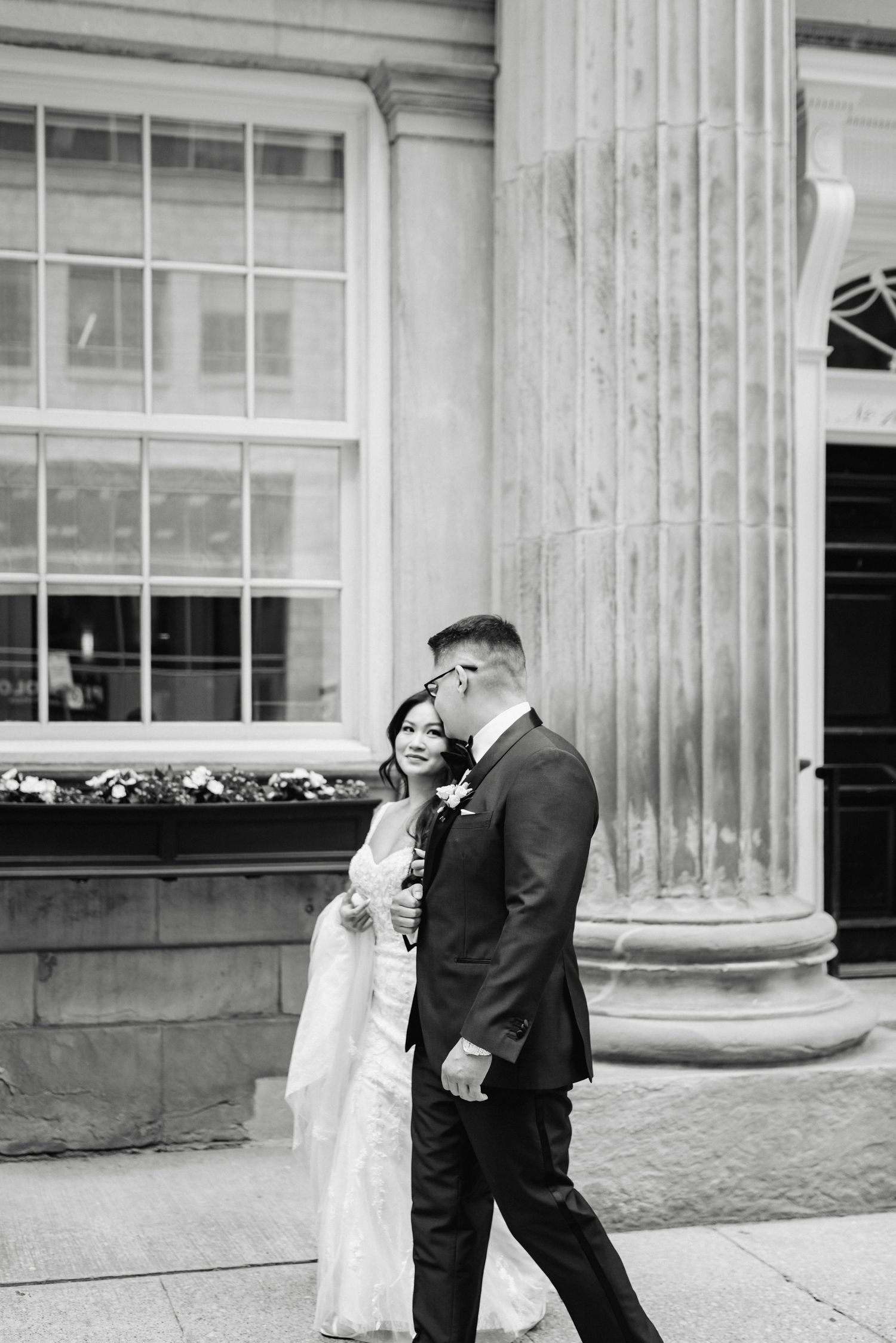 Wedding couple posing against classic stone columns of a historic building exterior.