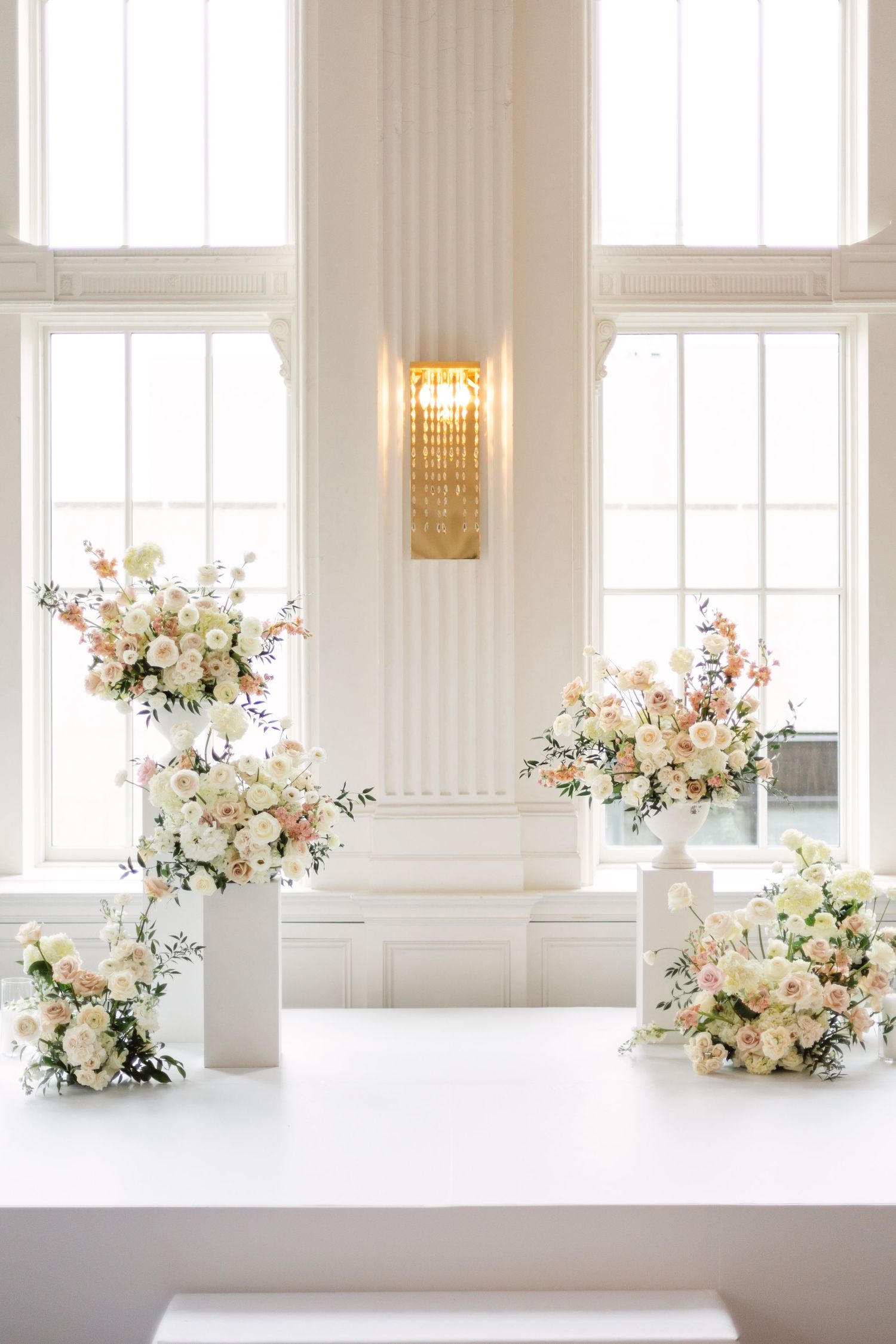 Romantic floral arrangements with blush and white flowers displayed along bright windows.