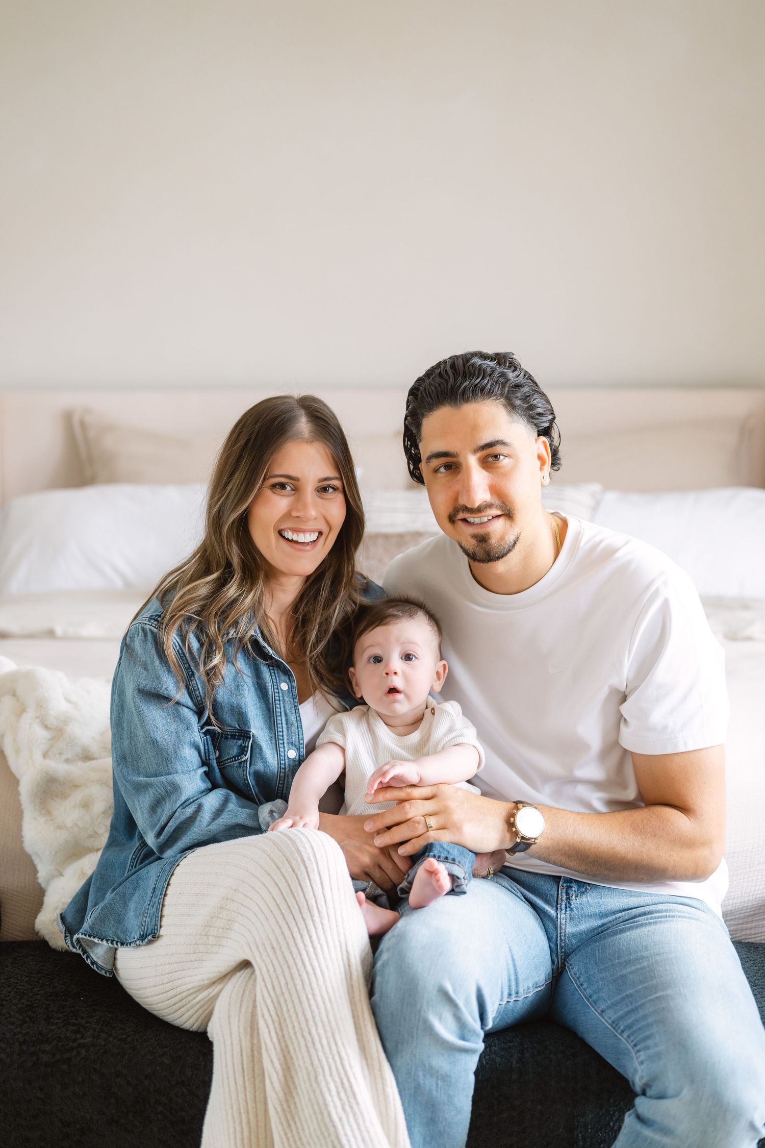Family in casual denim and white outfits lounging together on a couch during an indoor photo session.