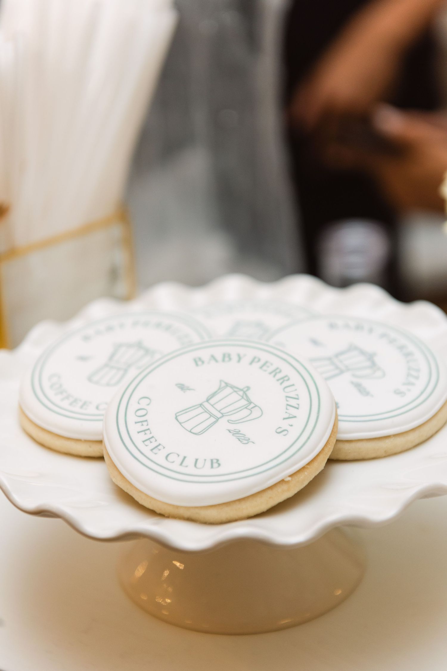 White frosted cookies with baby bottle design displayed on a scalloped cake stand.