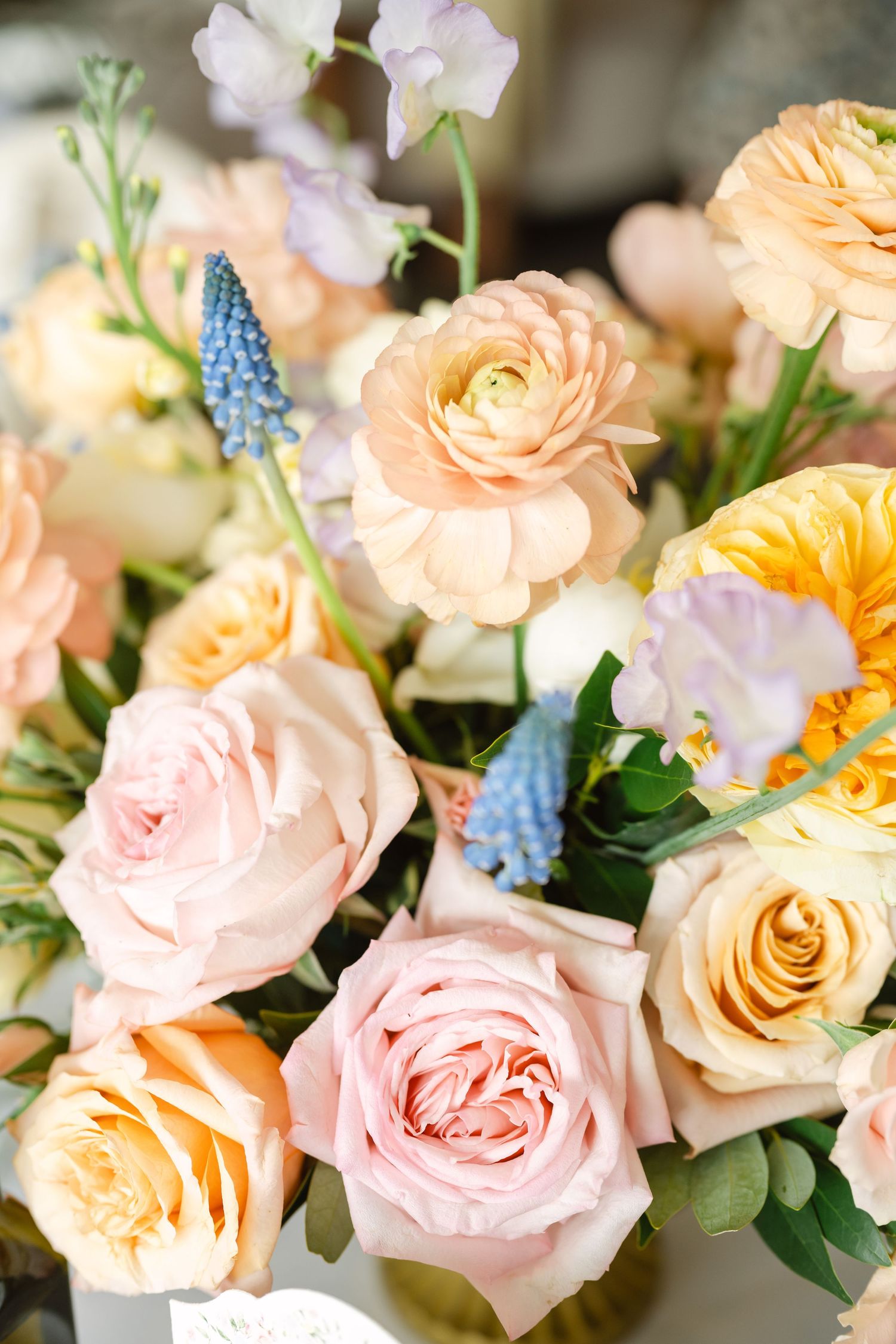 Close-up of a lush bridal bouquet featuring peach ranunculus, pink roses, yellow blooms, and purple muscari flowers.