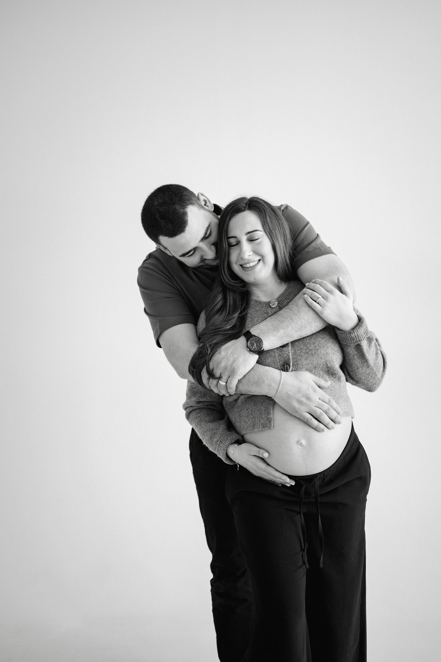 Intimate black and white maternity photo series showing tender embraces against white backdrop.