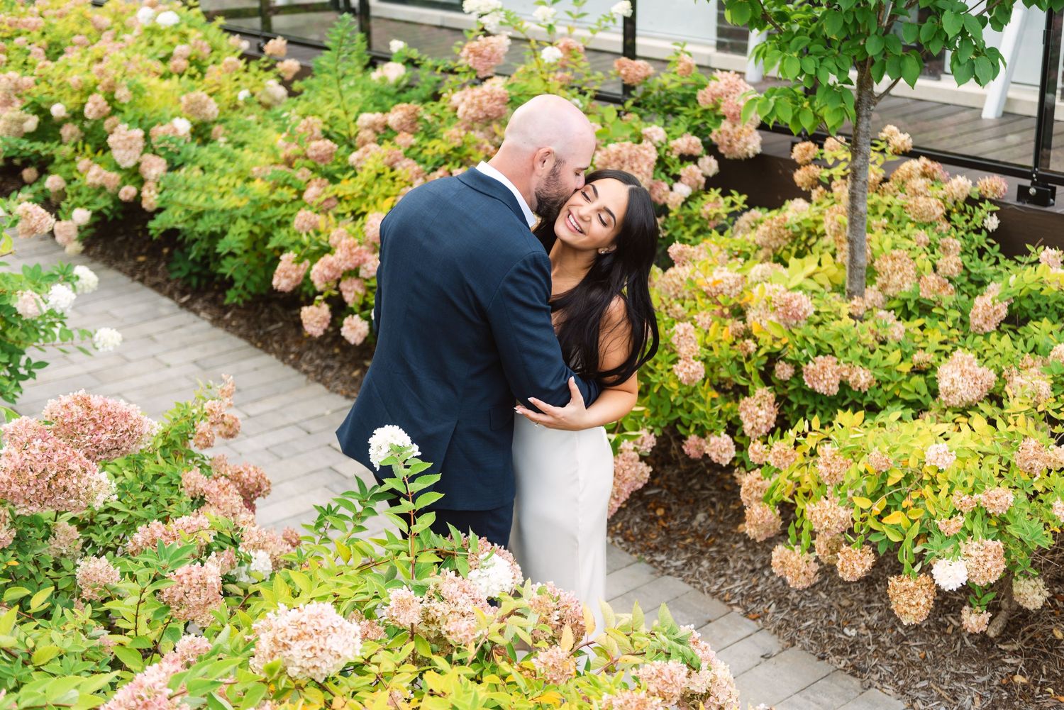 Couple embracing in lush garden surrounded by blooming hydrangea flowers.