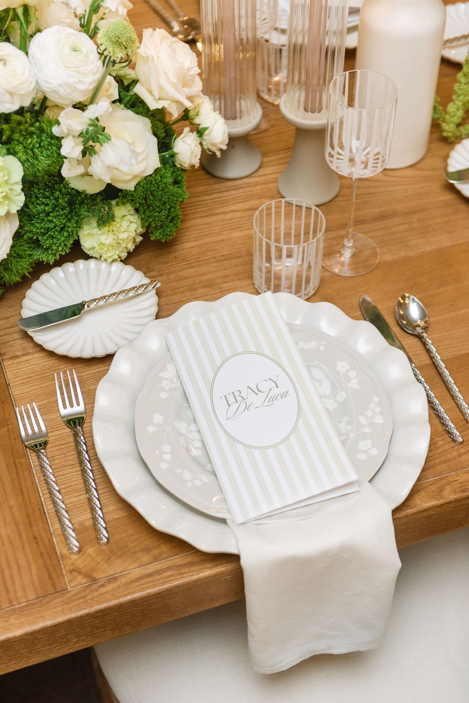 Elegant white and silver place settings on wooden table with floral centerpieces.
