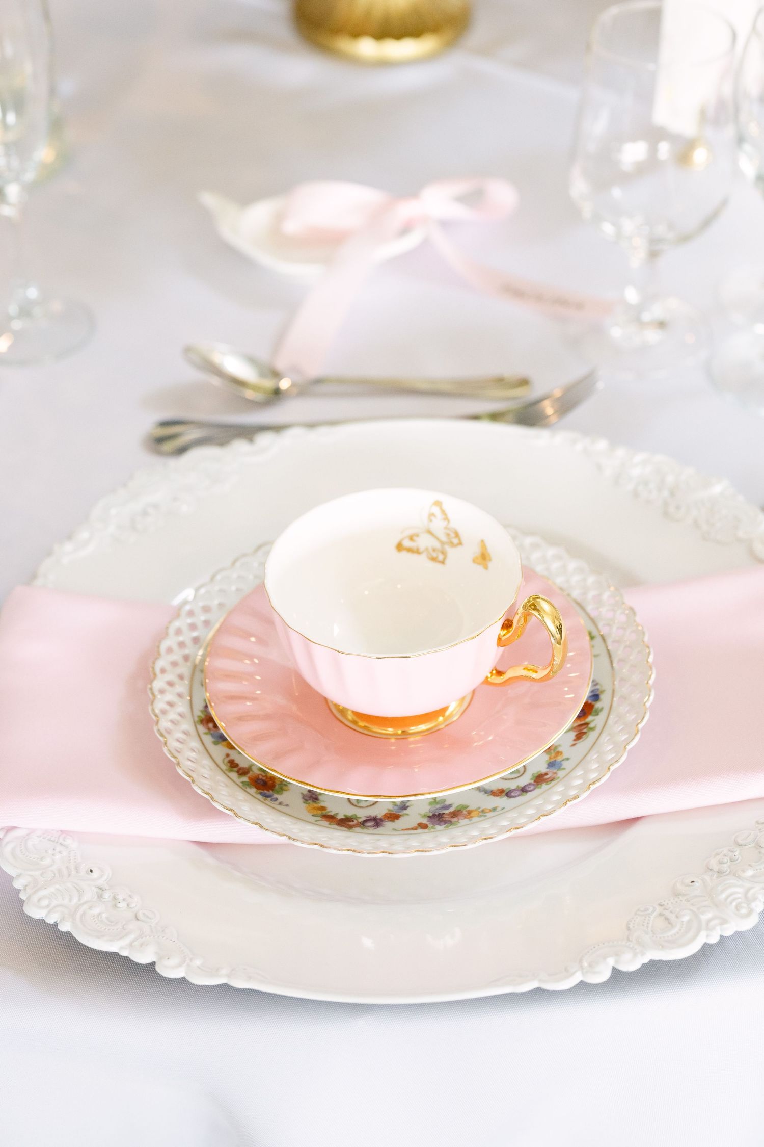 Elegant pink and white tea cup with gold butterfly detail on layered plates with pink ribbon napkin for a bridal shower.