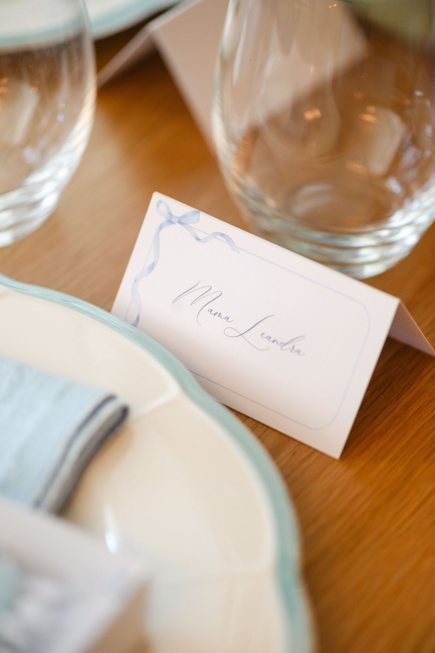 White place cards with handwritten names sit beside elegant table settings on a wooden dining surface.