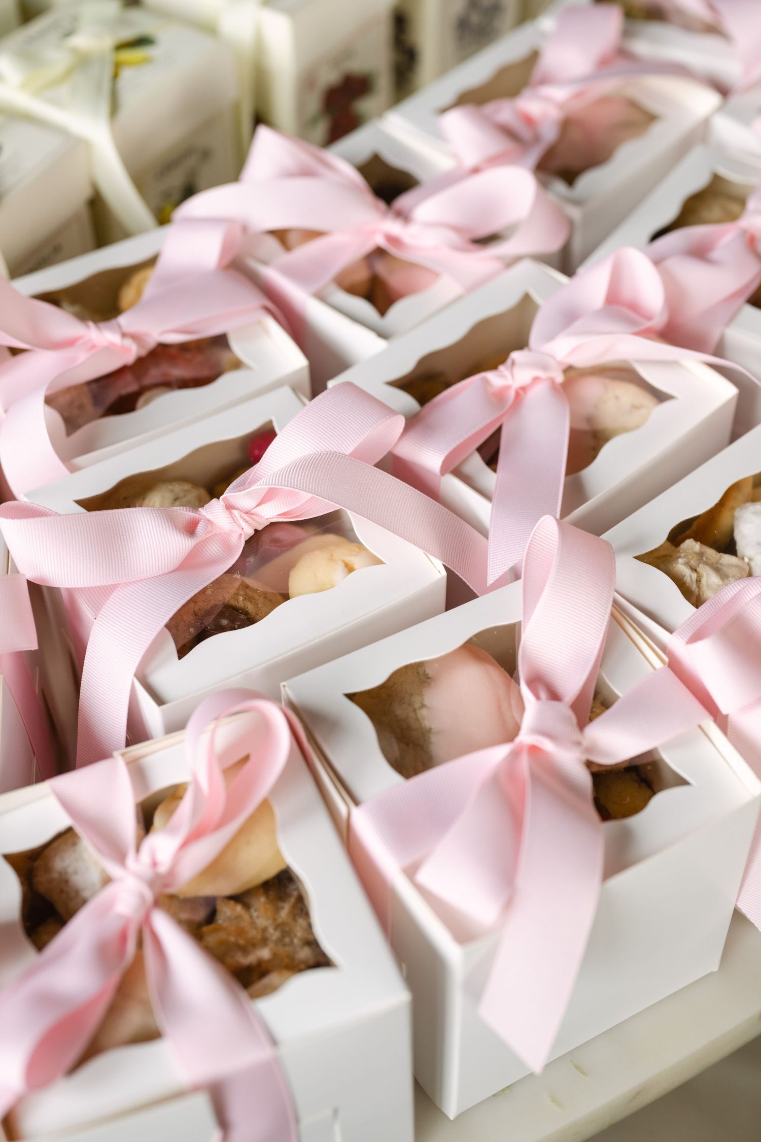White gift boxes with pink satin ribbon bows containing assorted chocolates and truffles, perfect for wedding favors.