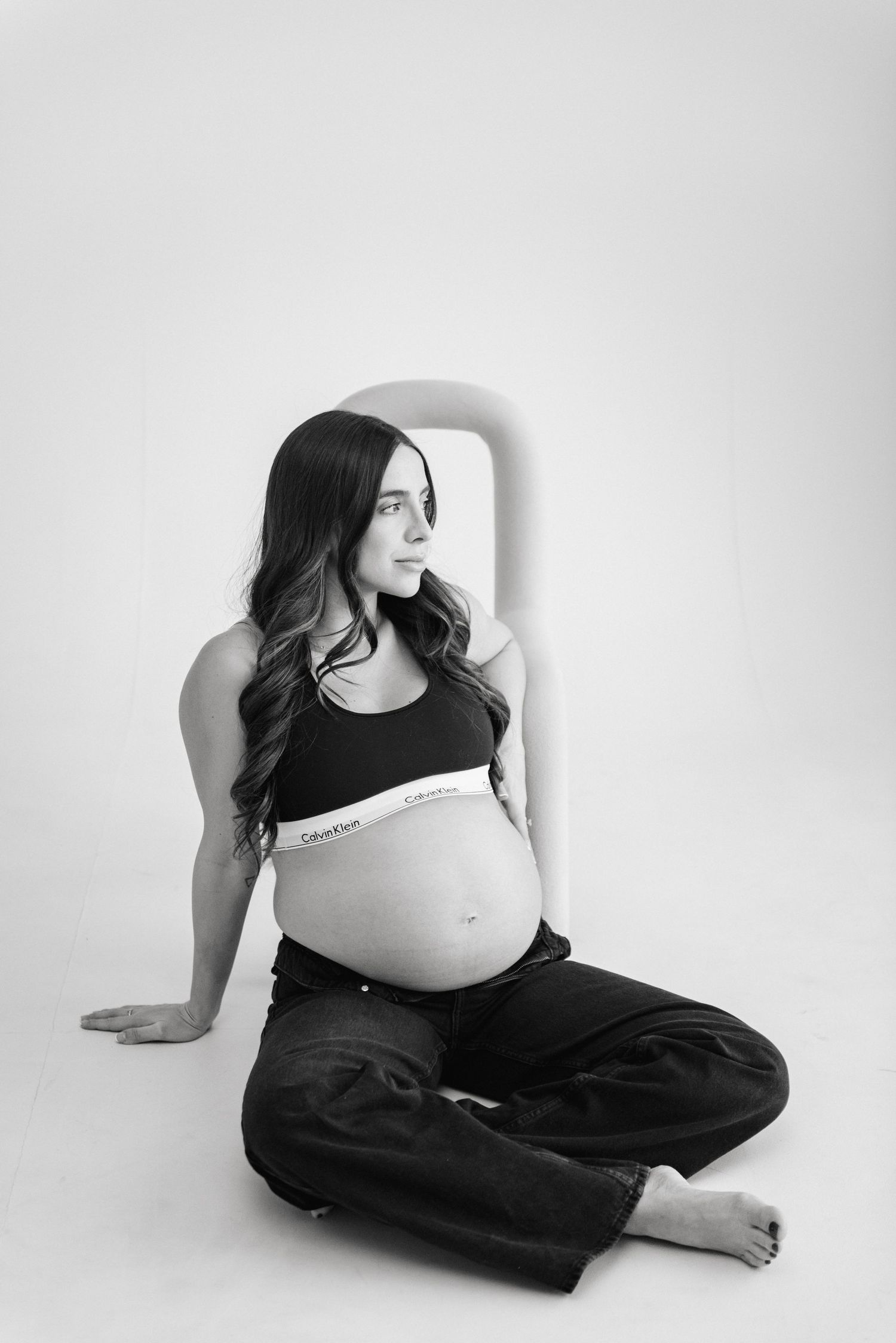 Black and white portrait of expectant mother in casual attire against light background.
