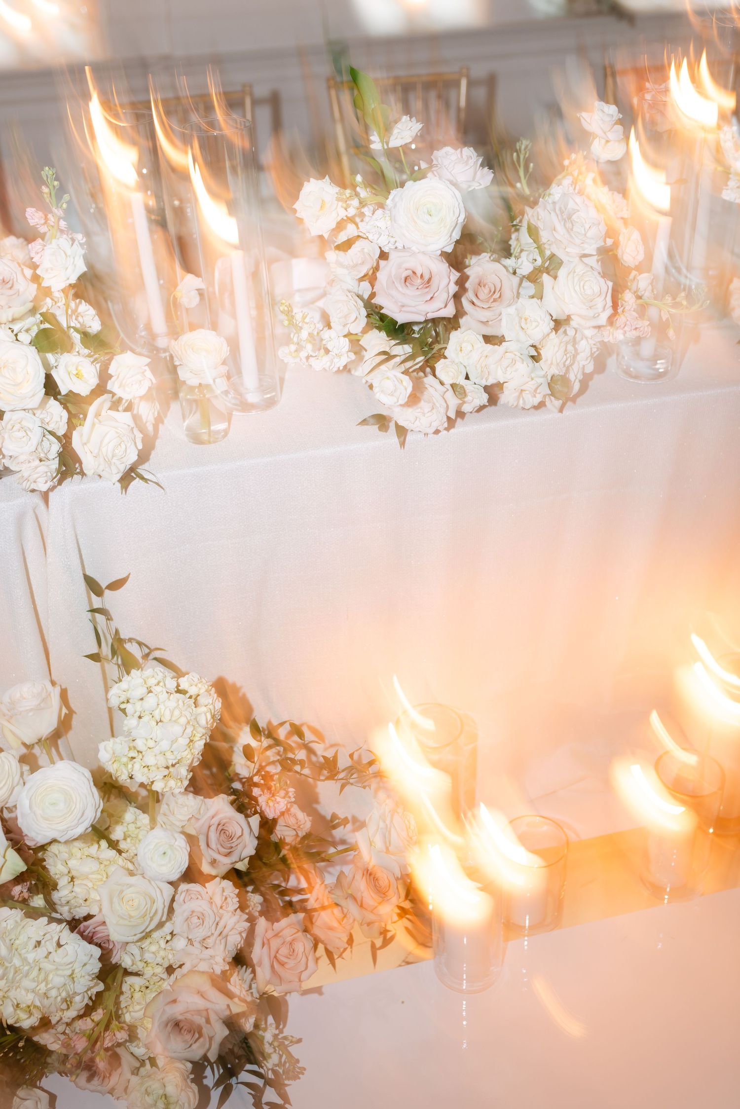 White and blush floral arrangements with glowing candles creating romantic wedding table decor.