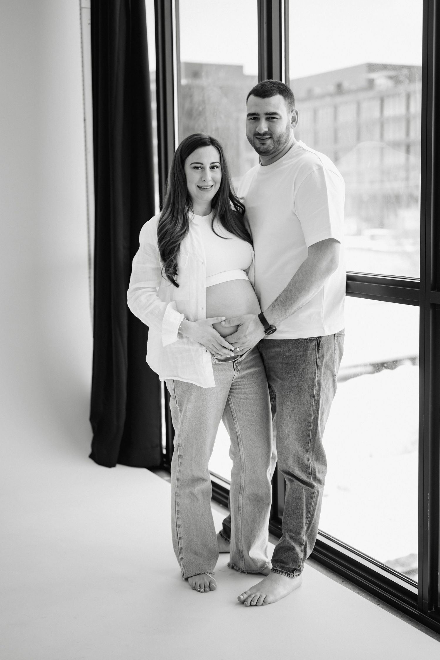 Black and white minimalist photo showing two people in white and denim against a window backdrop.