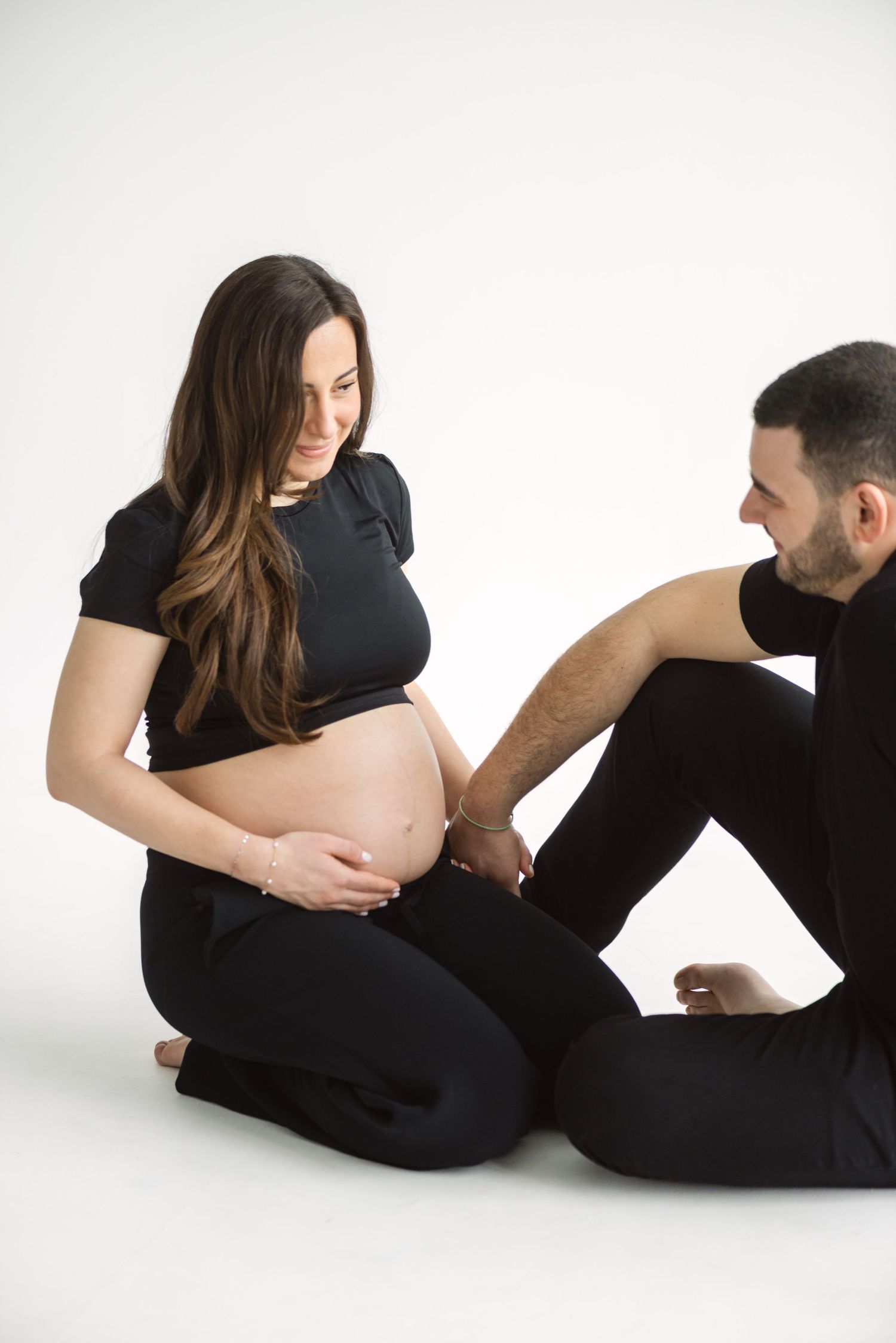 Two people in black clothing pose together in a series of intimate artistic portraits against a white backdrop.