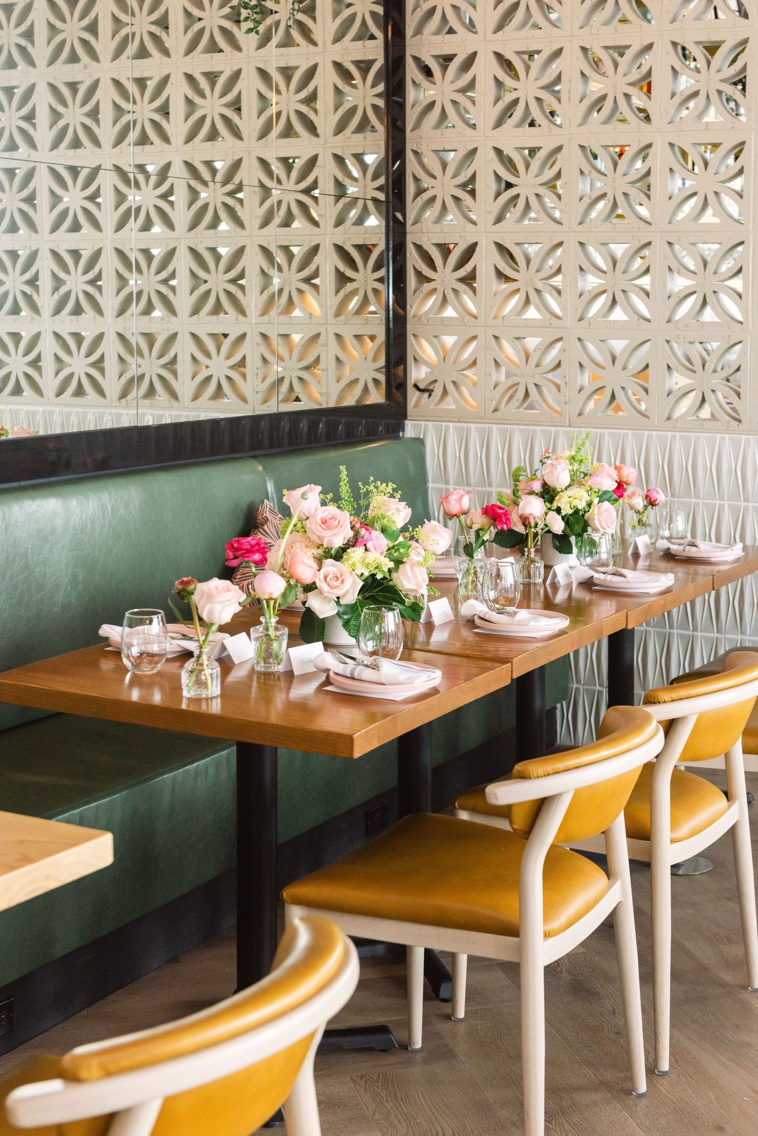 Elegant restaurant booth with green leather seating, wooden tables, pink floral centerpieces, and decorative lattice wall panels.