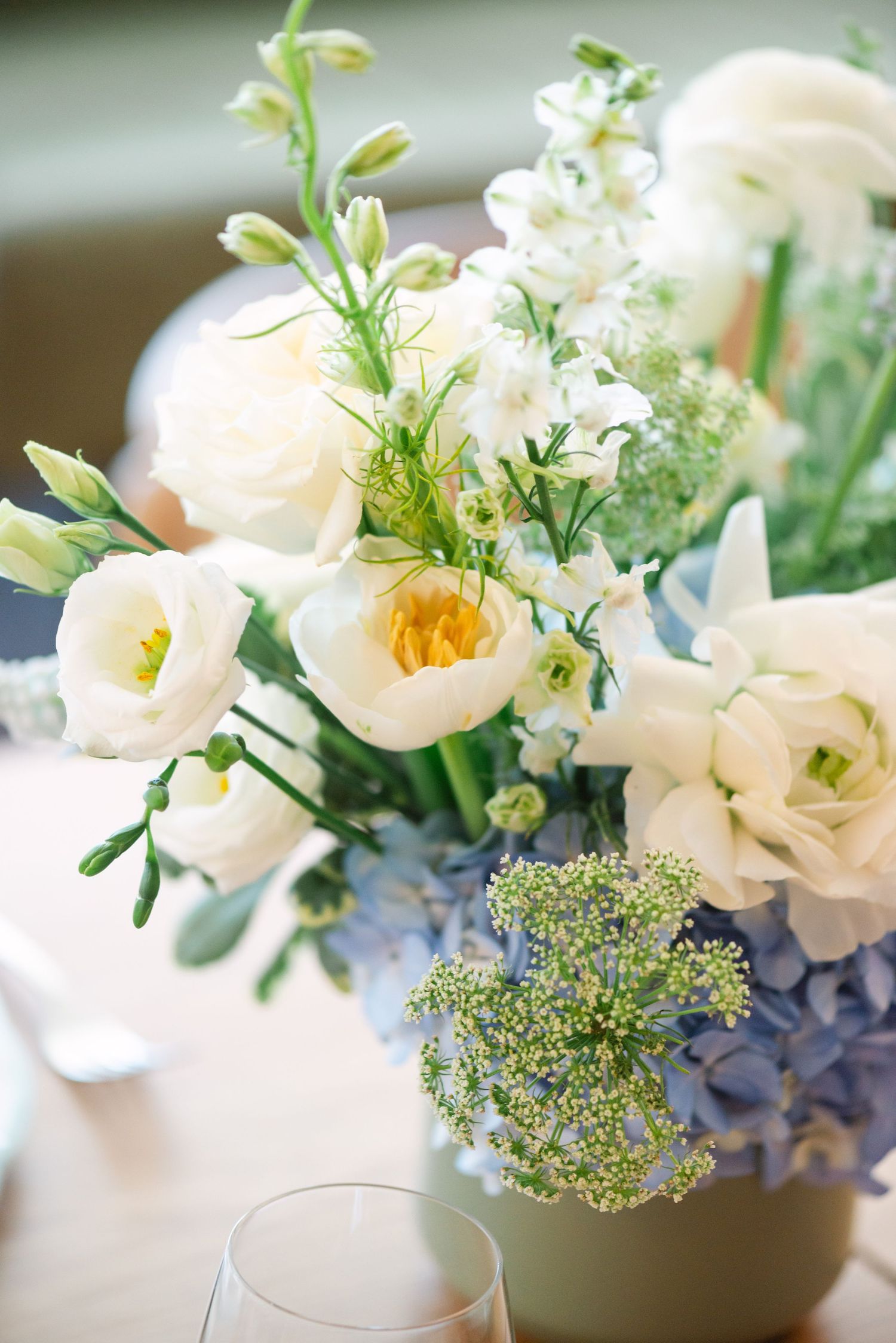 Delicate white flowers with blue hydrangeas and greenery arranged in elegant vases create a soft spring centerpiece display.
