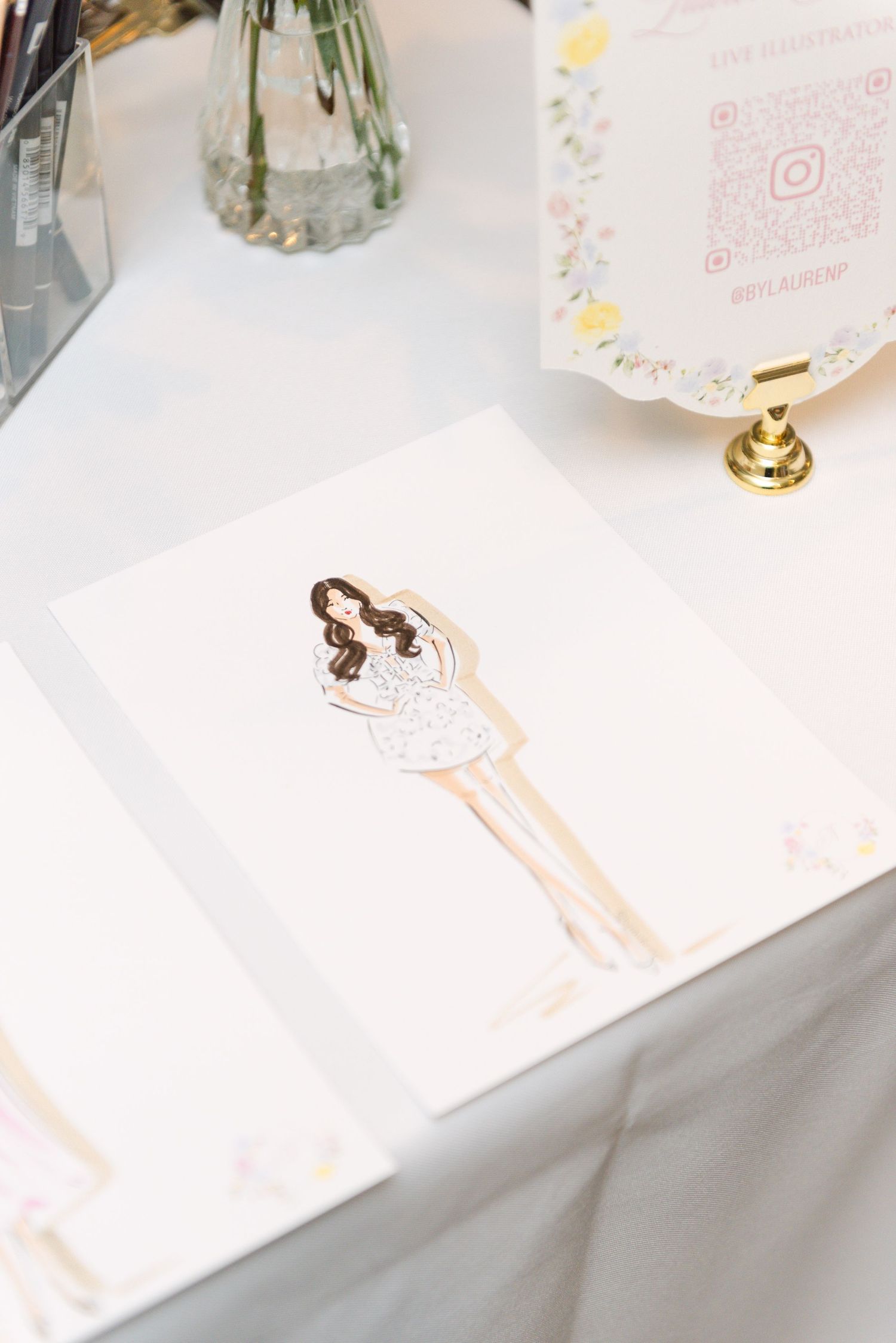 Illustrated portrait card of brunette bride in white dress displayed on table at bridal shower event.