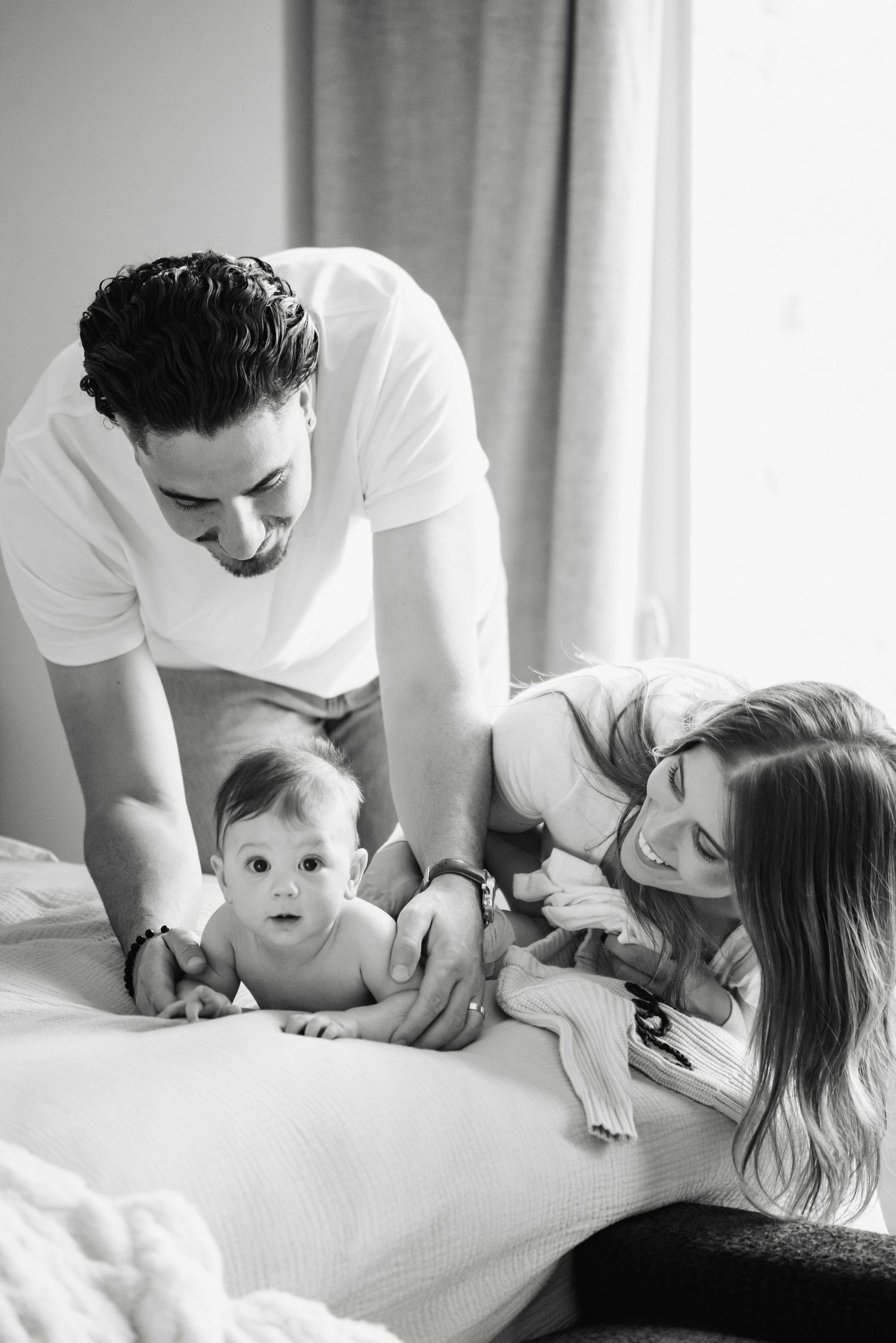 Black and white photo series showing tender family moments between parent and child on a white bed.