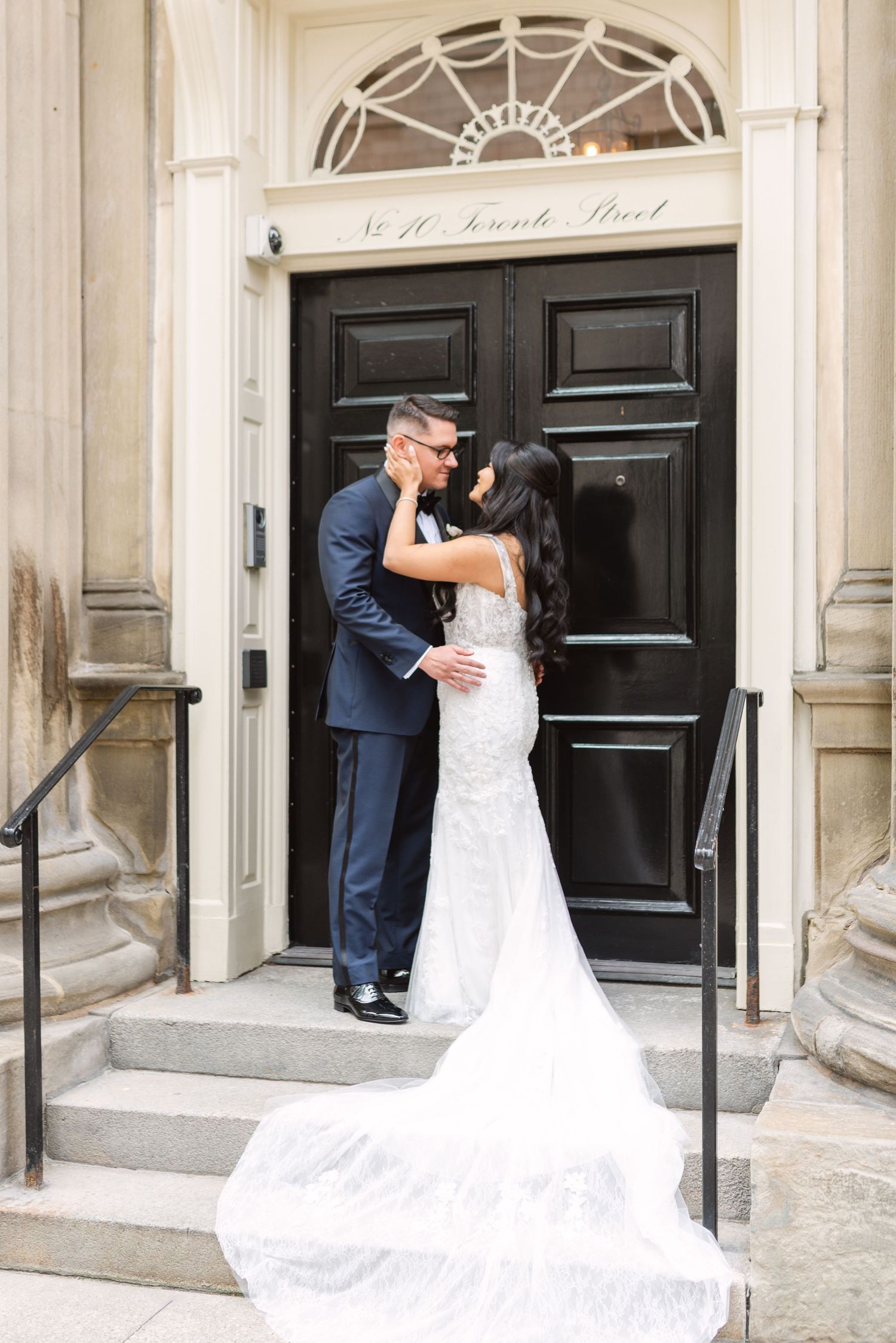 A wedding couple poses in front of a grand black door with elegant architectural details.
