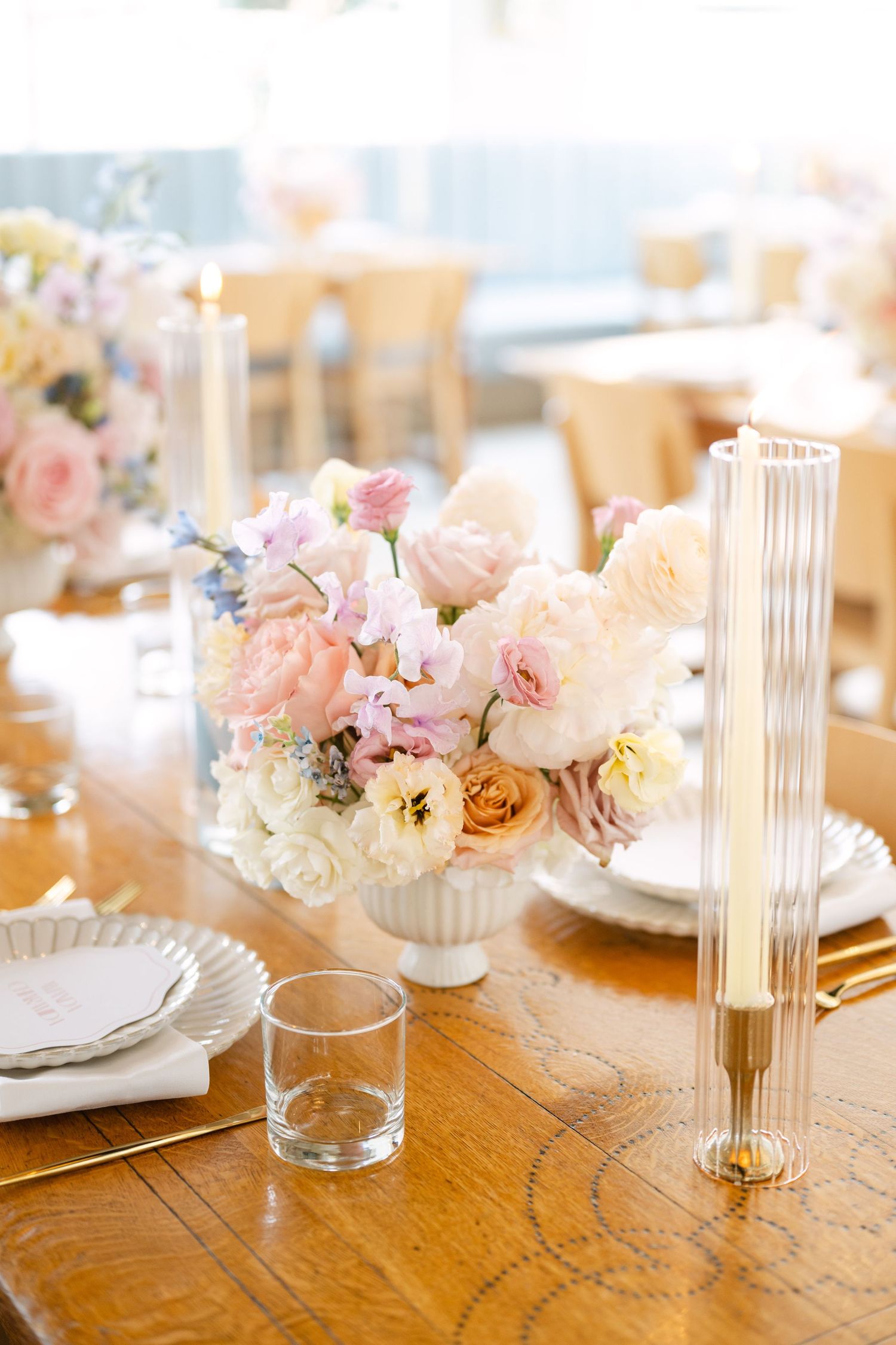 Elegant table setting with pink floral centerpieces and gold accents on a wooden dining table.