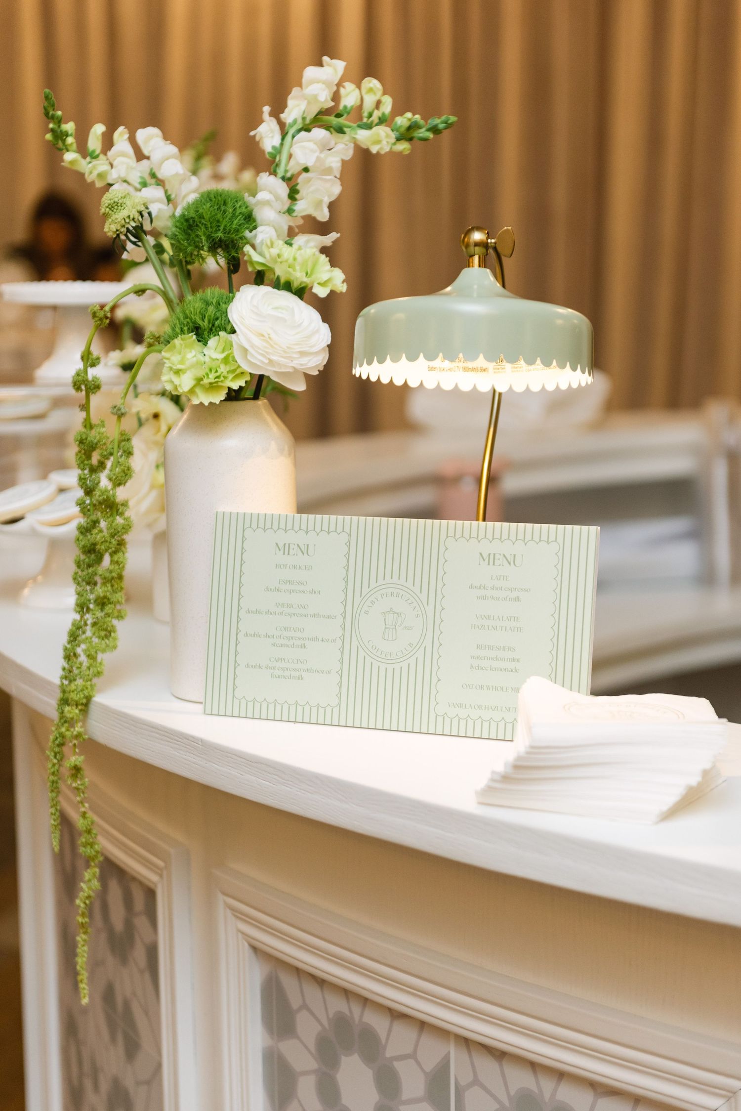 Mint green wedding menu cards displayed with white floral arrangement and decorative lamp.
