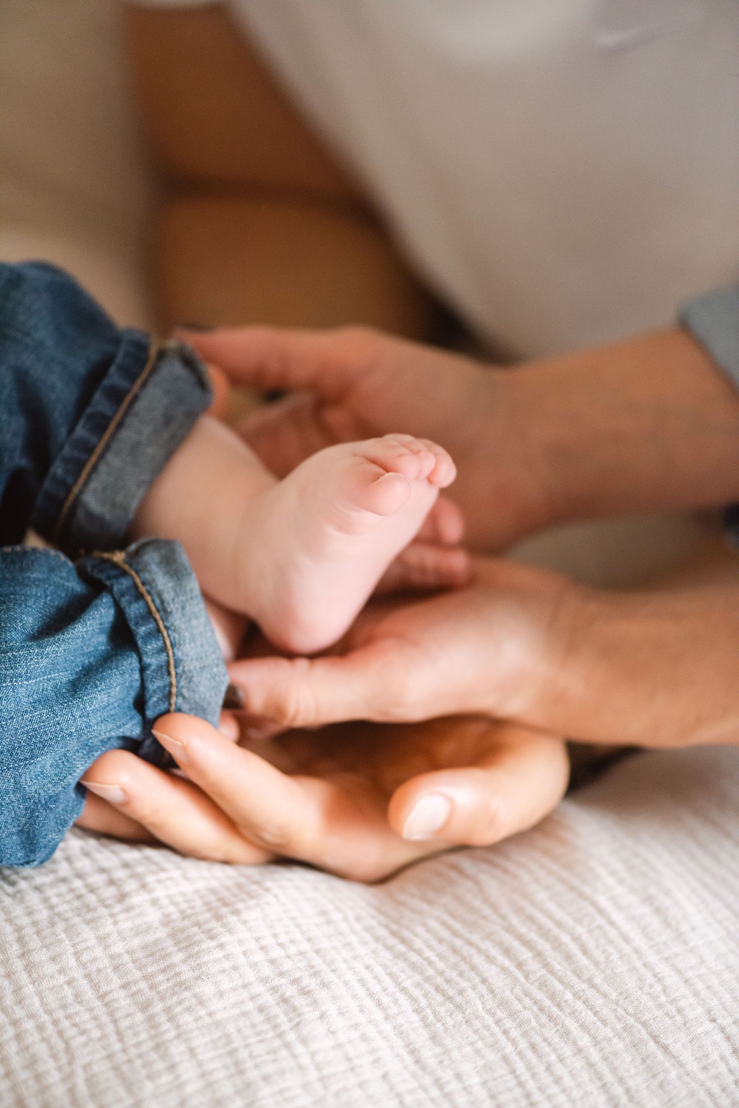 Close up of tiny baby foot being gently held in adult hands on white fabric.