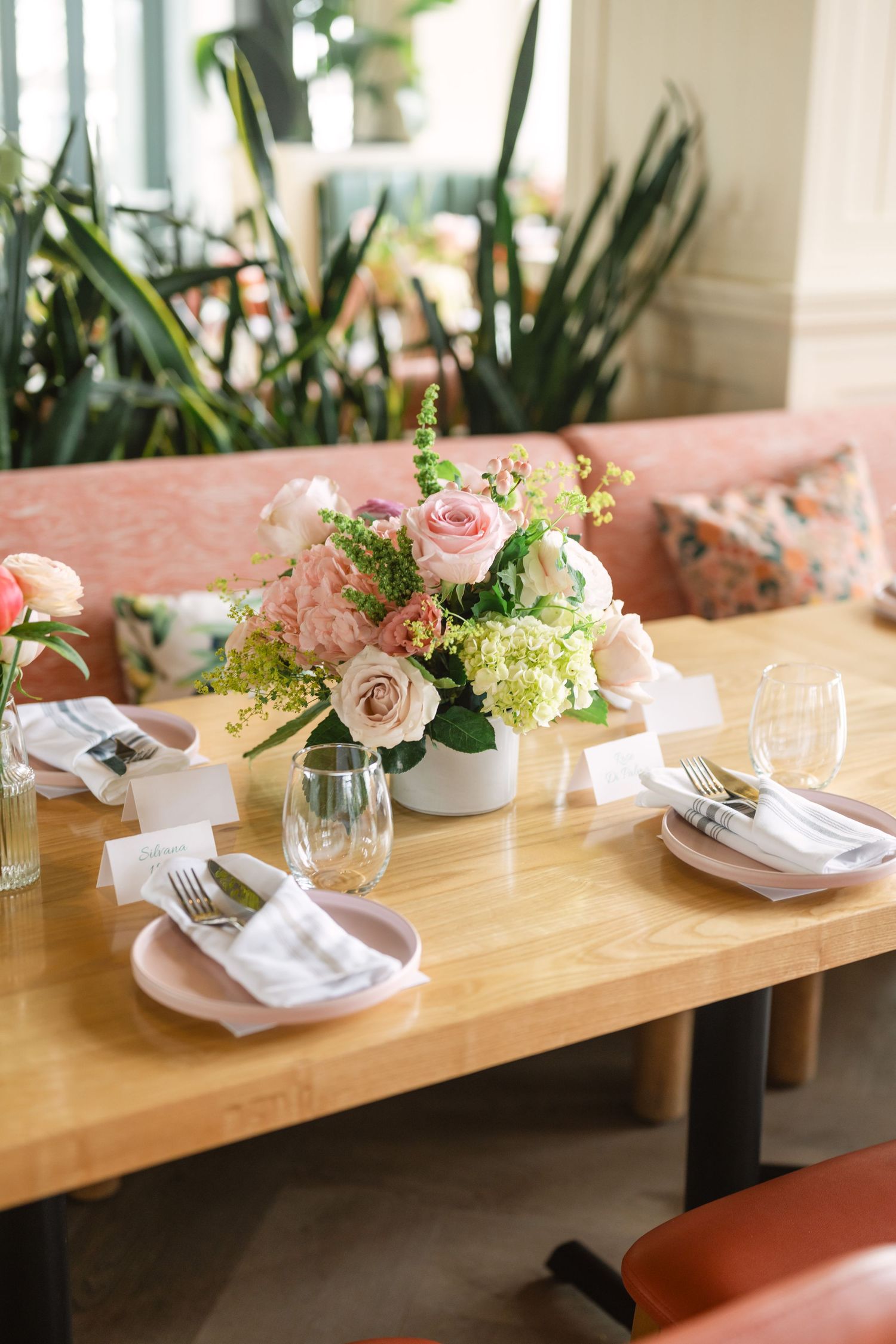 Elegant restaurant table setting with pink roses, hydrangeas, place cards, and gold cutlery.
