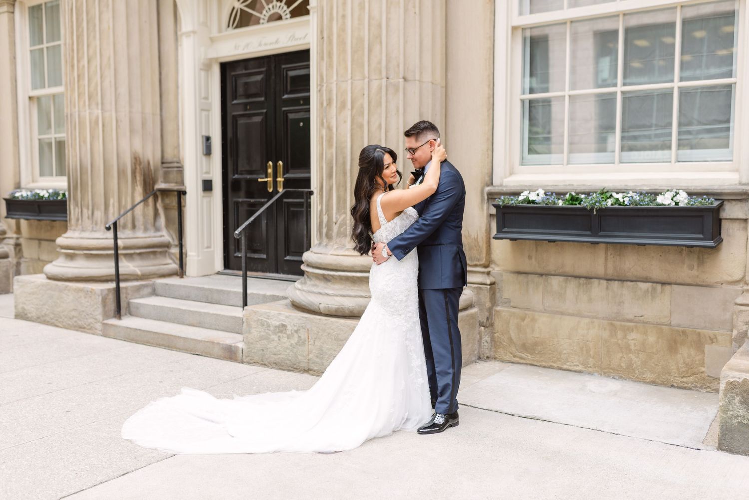 A romantic wedding moment captured in front of an elegant stone building with classic architecture.
