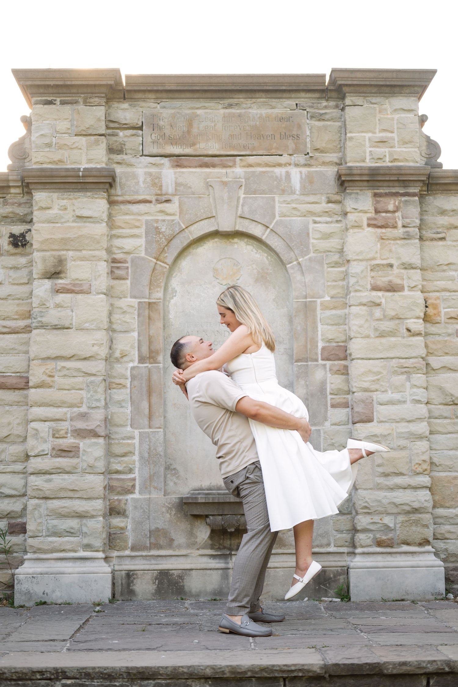 Playful dance lift pose against a historic stone wall backdrop.